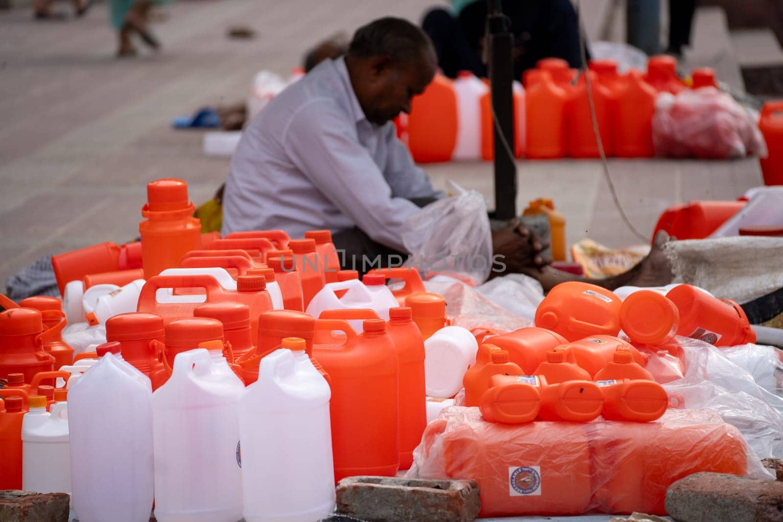 Shopkeeper selling saffron white water bottles used to fill holy water from river ganga for prayers and rituals by Shalinimathur