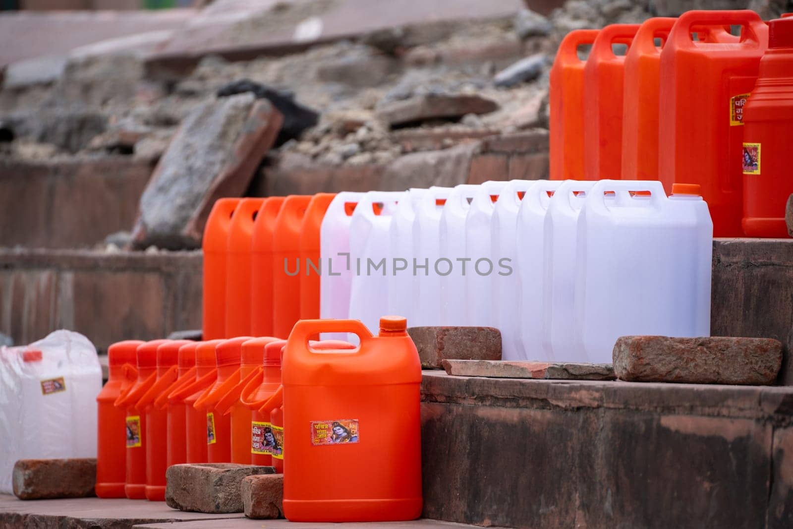 colorful plastic cans in orange saffron and white showing the traditional vessels used to fill holy water from ganga river to take home in India