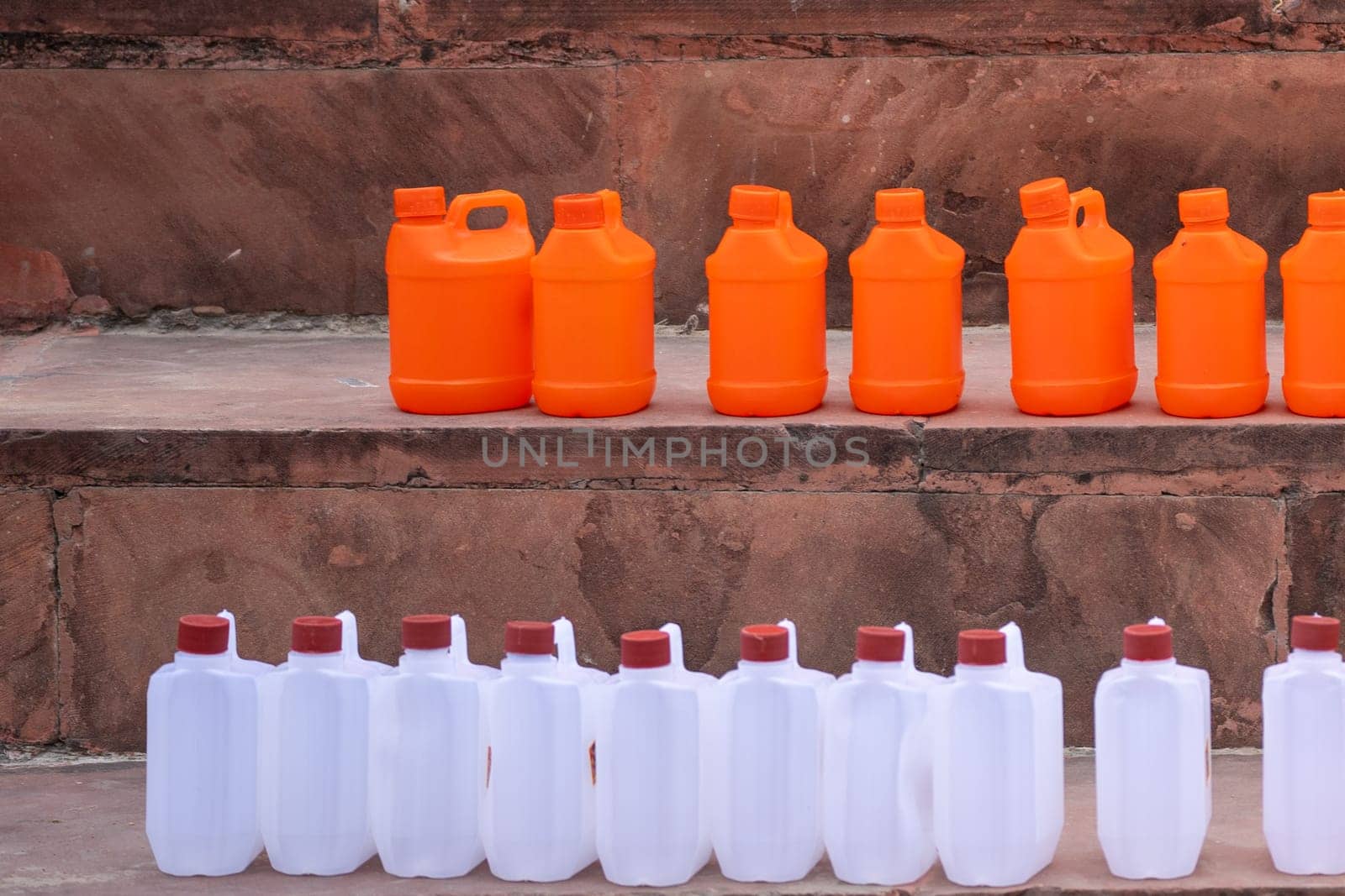 colorful plastic cans in orange saffron and white showing the traditional vessels used to fill holy water from ganga river to take home by Shalinimathur