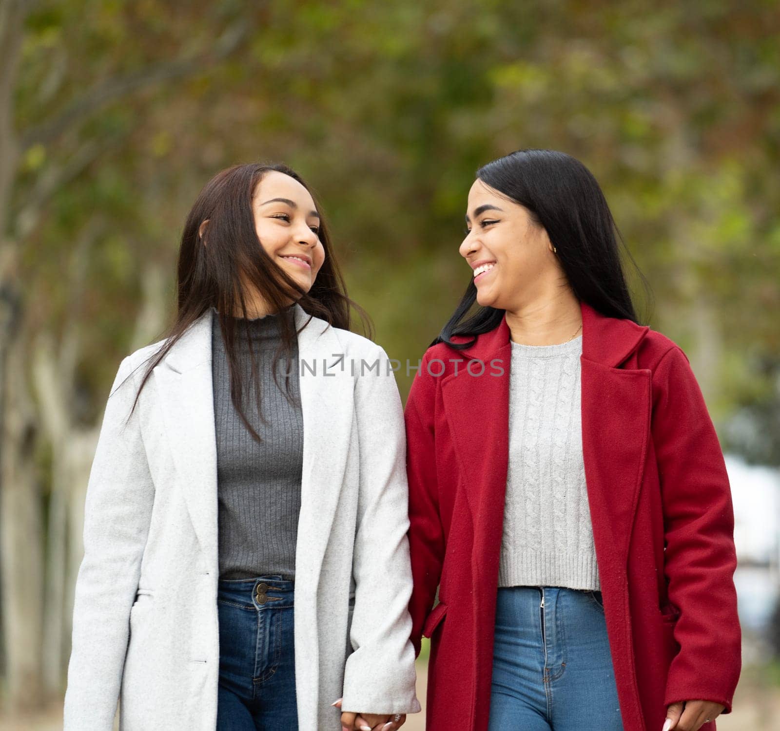 Front view of lesbian latin couple in love smiling looking at each other , holding hands in a park.LGBT family.