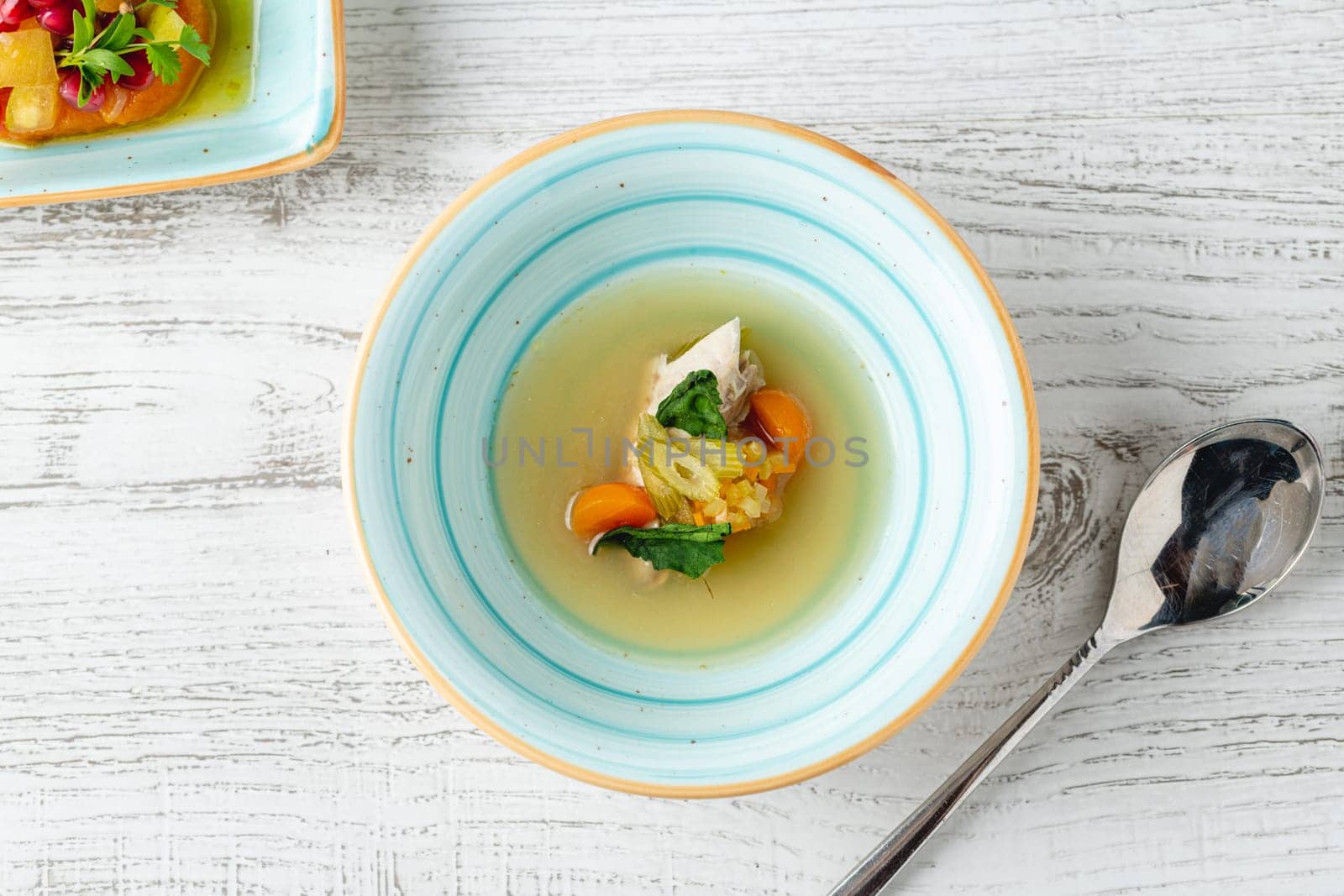 Fish soup with vegetables on white wooden table by Sonat