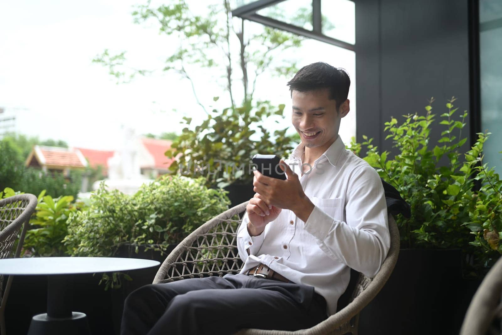 Portrait of smiling adult businessman using mobile phone at office terrace.