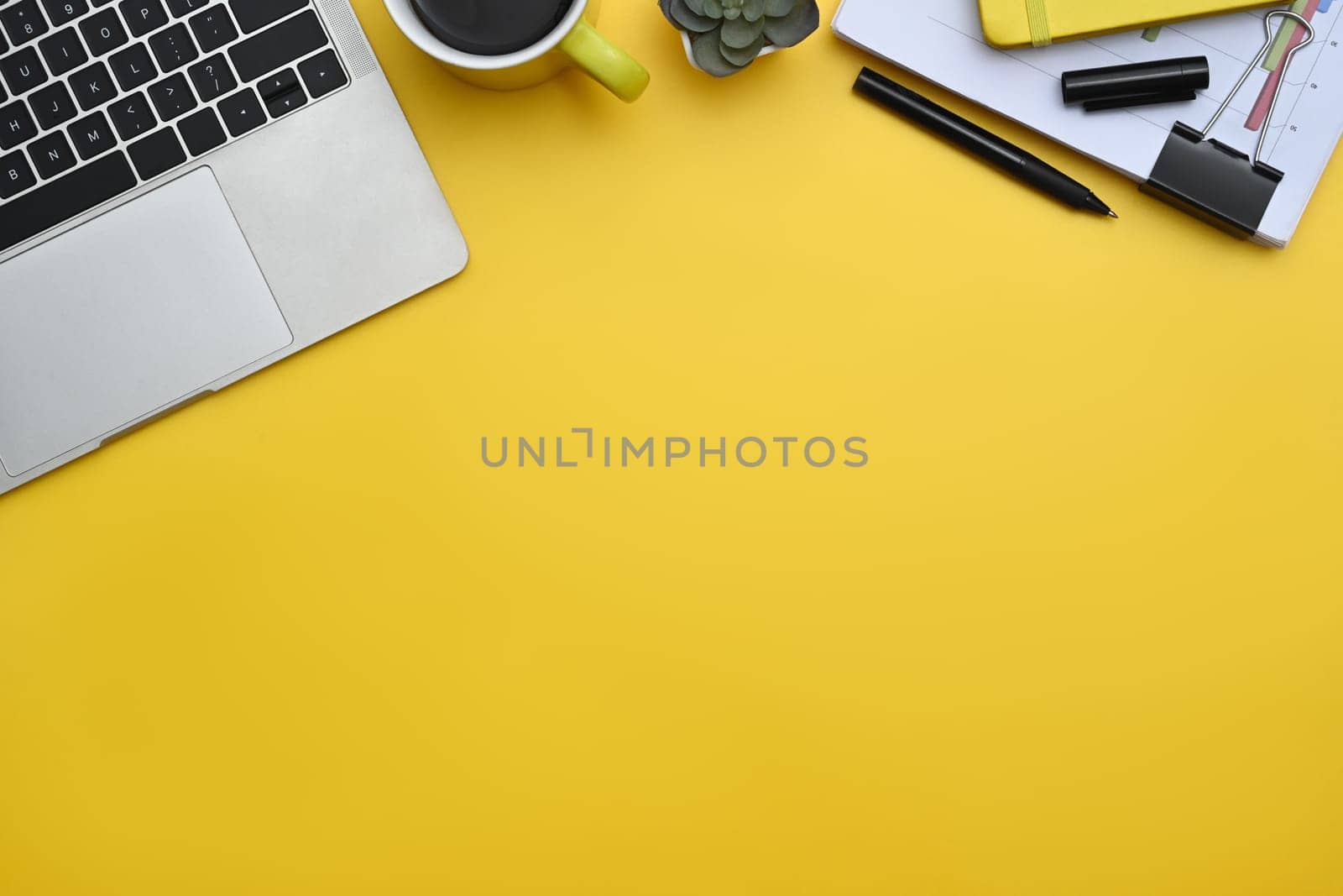 Top view of laptop, coffee cup and documents on yellow background with copy space.