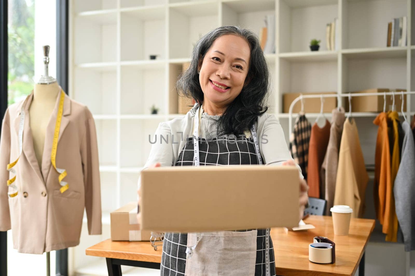 Portrait of senior woman small business owner holding parcel box and smiling to camera by prathanchorruangsak