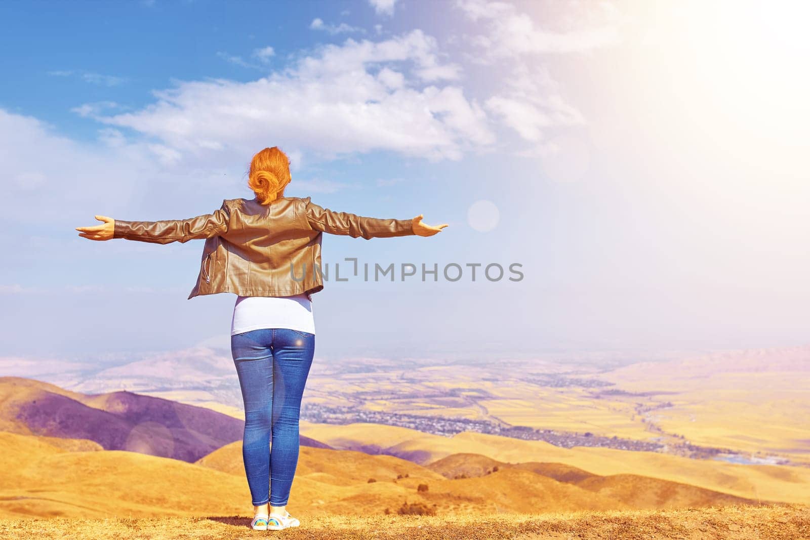 Beauty woman outdoors enjoying nature. A tourist girl on a mountain and looks at the sunrise and spread arms.