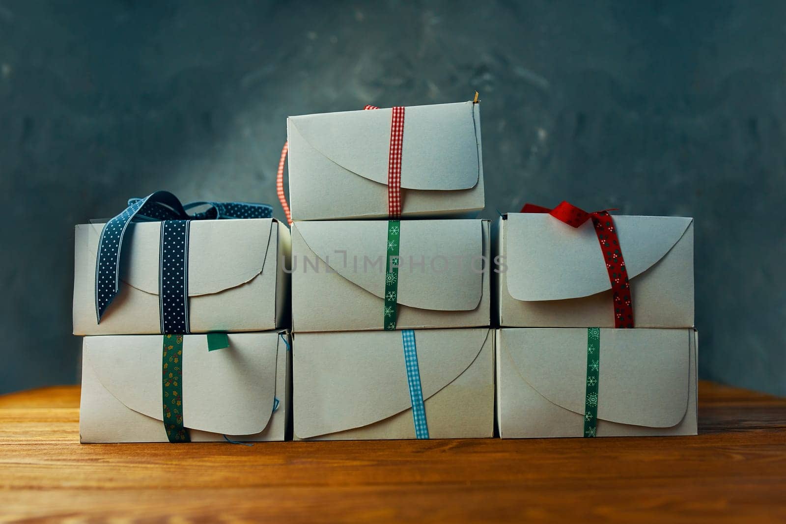 Stack of gift wrapped Christmas presents. A stack of gifts of white colors tied with different ribbons on a wooden background.