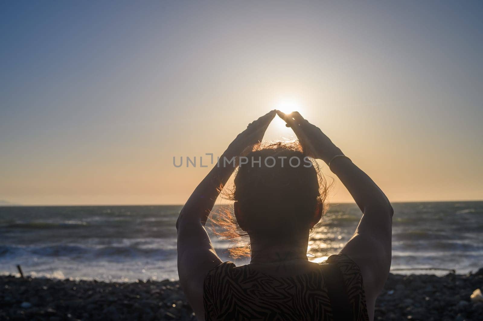 Silhouette of a woman holding the sun in her hands. On the seashore at sunset.