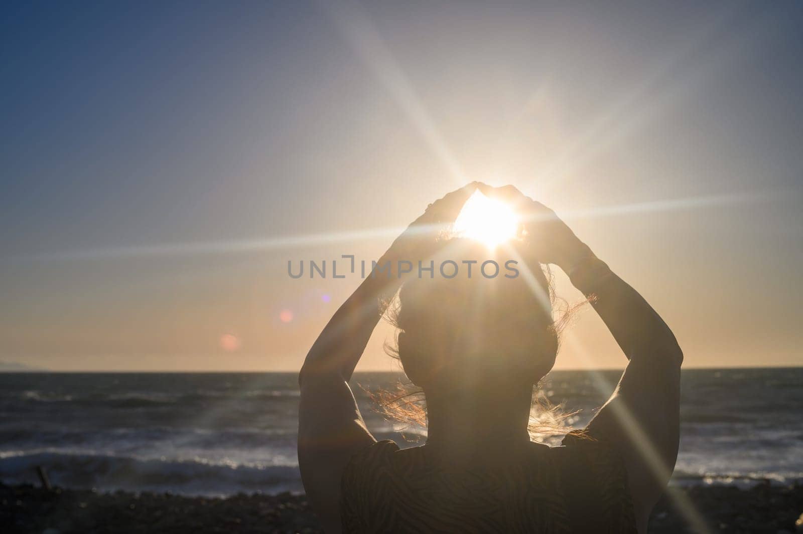 Silhouette of a woman holding the sun in her hands. On the seashore at sunset. by Mixa74