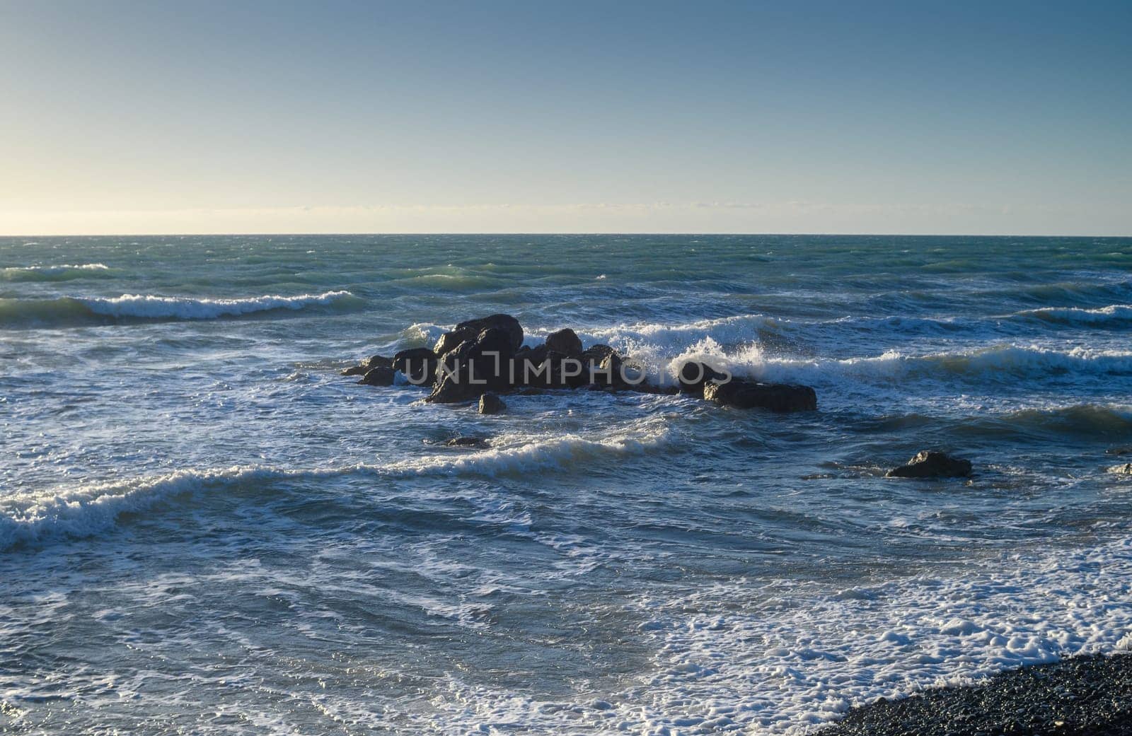 waves crash on large rocks in the Mediterranean Sea near the beach