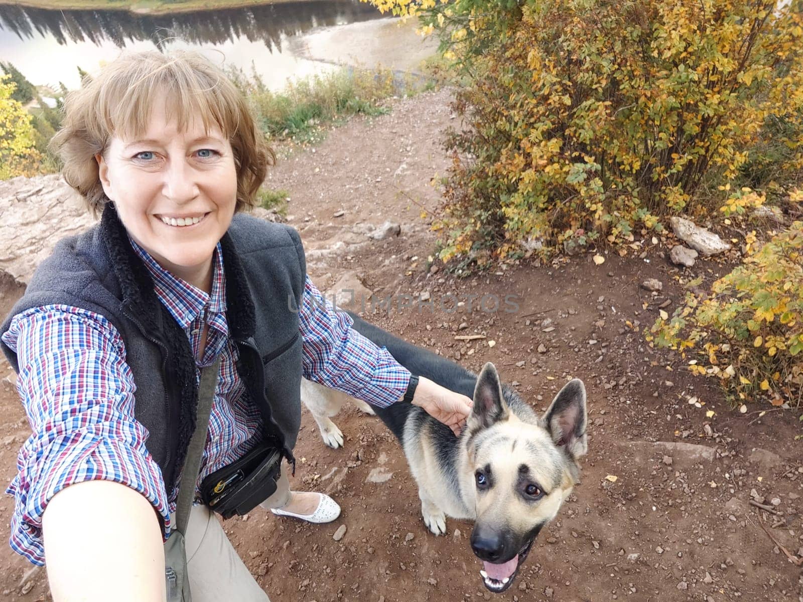 Adult girl or middle aged woman with shepherd dog on top of mountain. Walk on nature. Tourist and travel