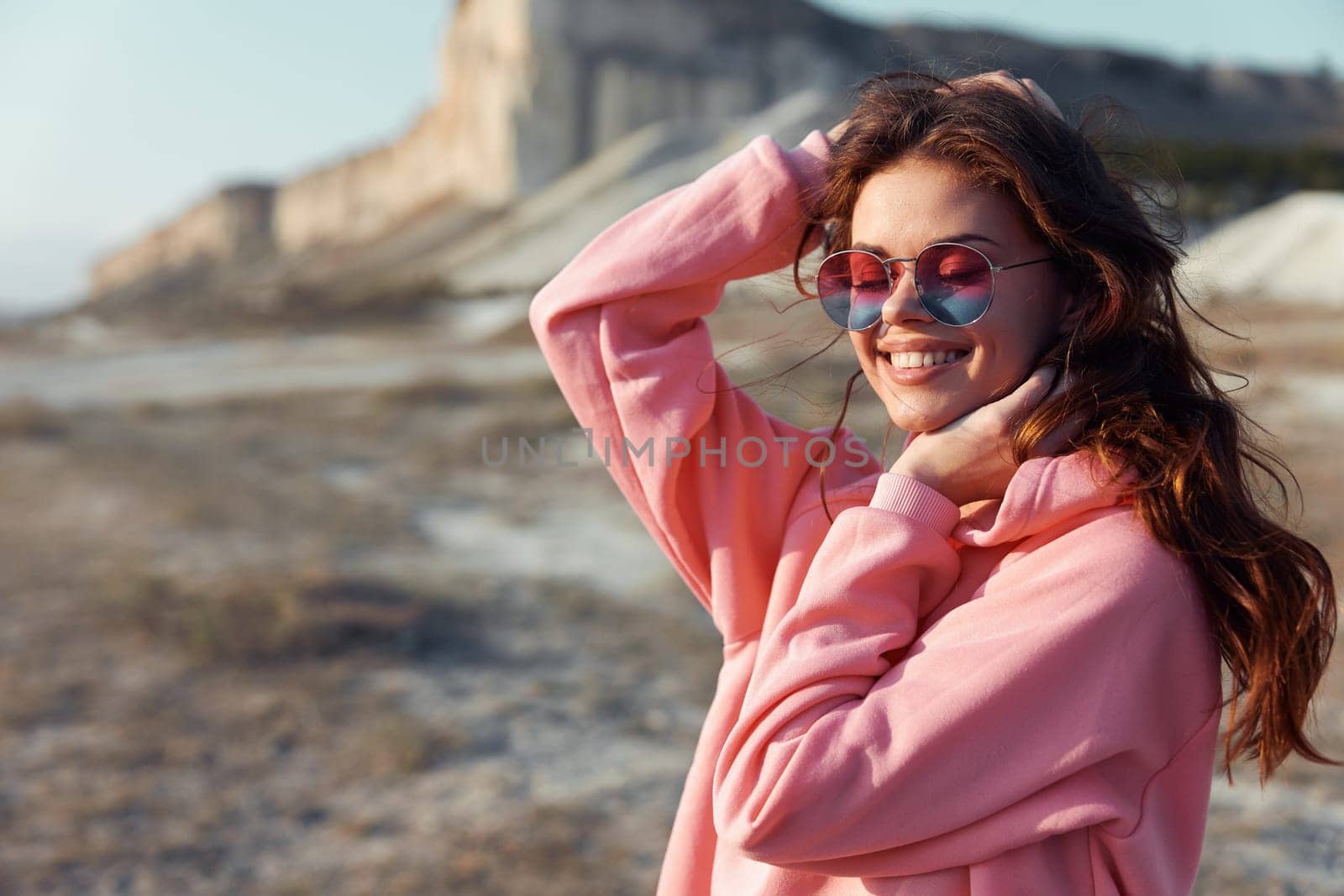 Serene woman in pink sweatshirt and sunglasses enjoying the view of a mountain from the beach by Vichizh