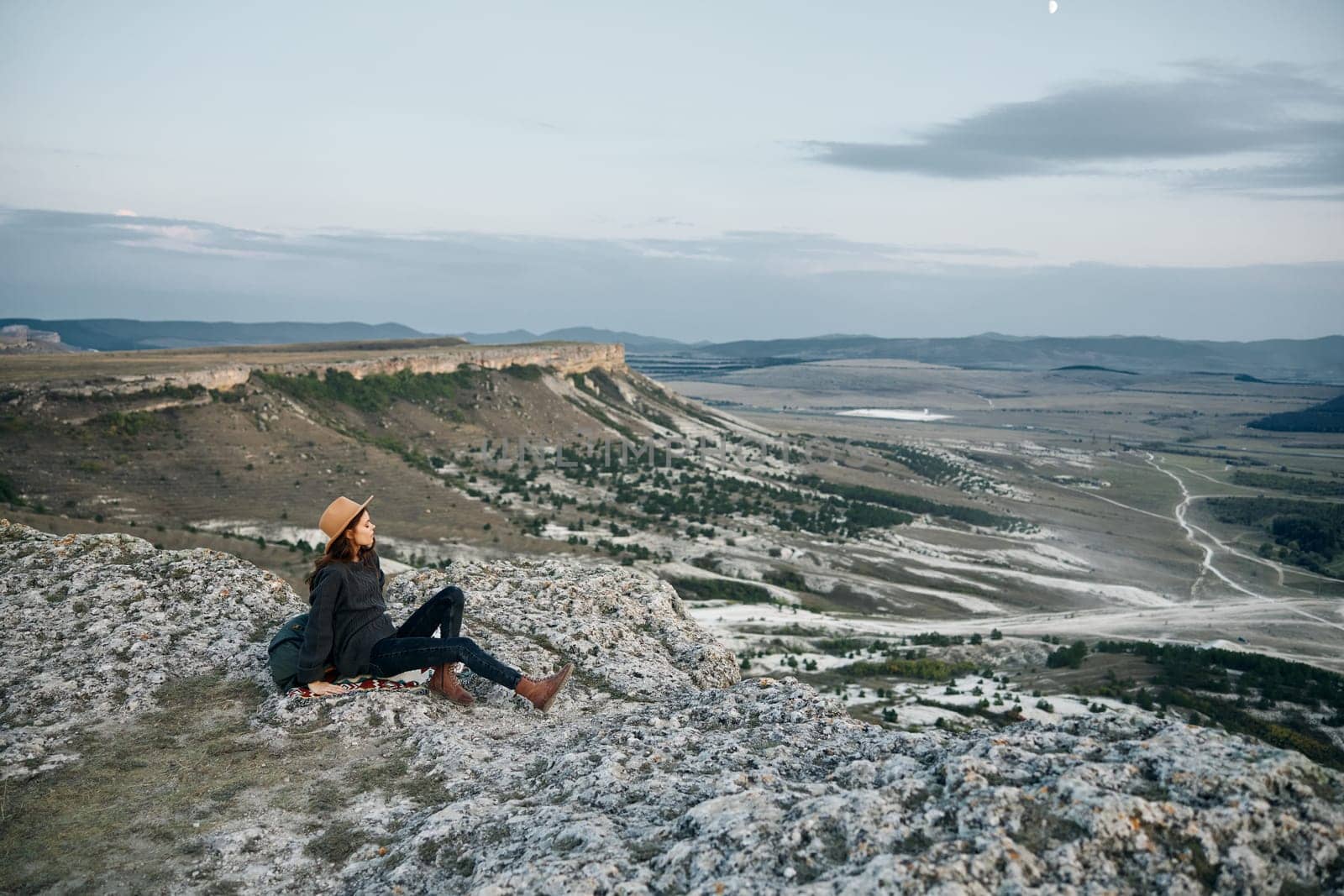 Serene woman sitting on rock gazes at majestic sunset over valley with mountains in background by Vichizh