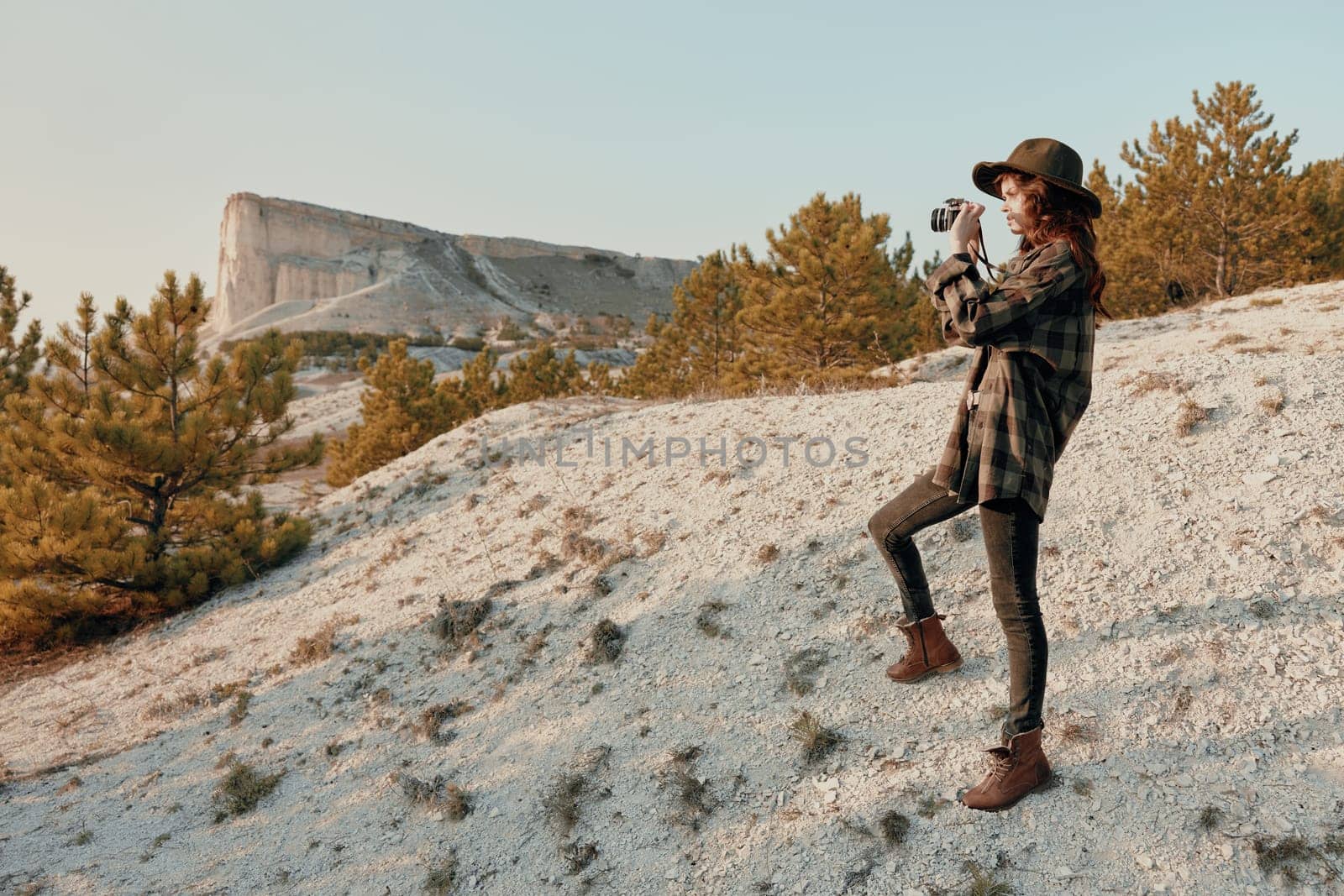 Woman in hat and plaid shirt standing on hilltop with mountain in background by Vichizh