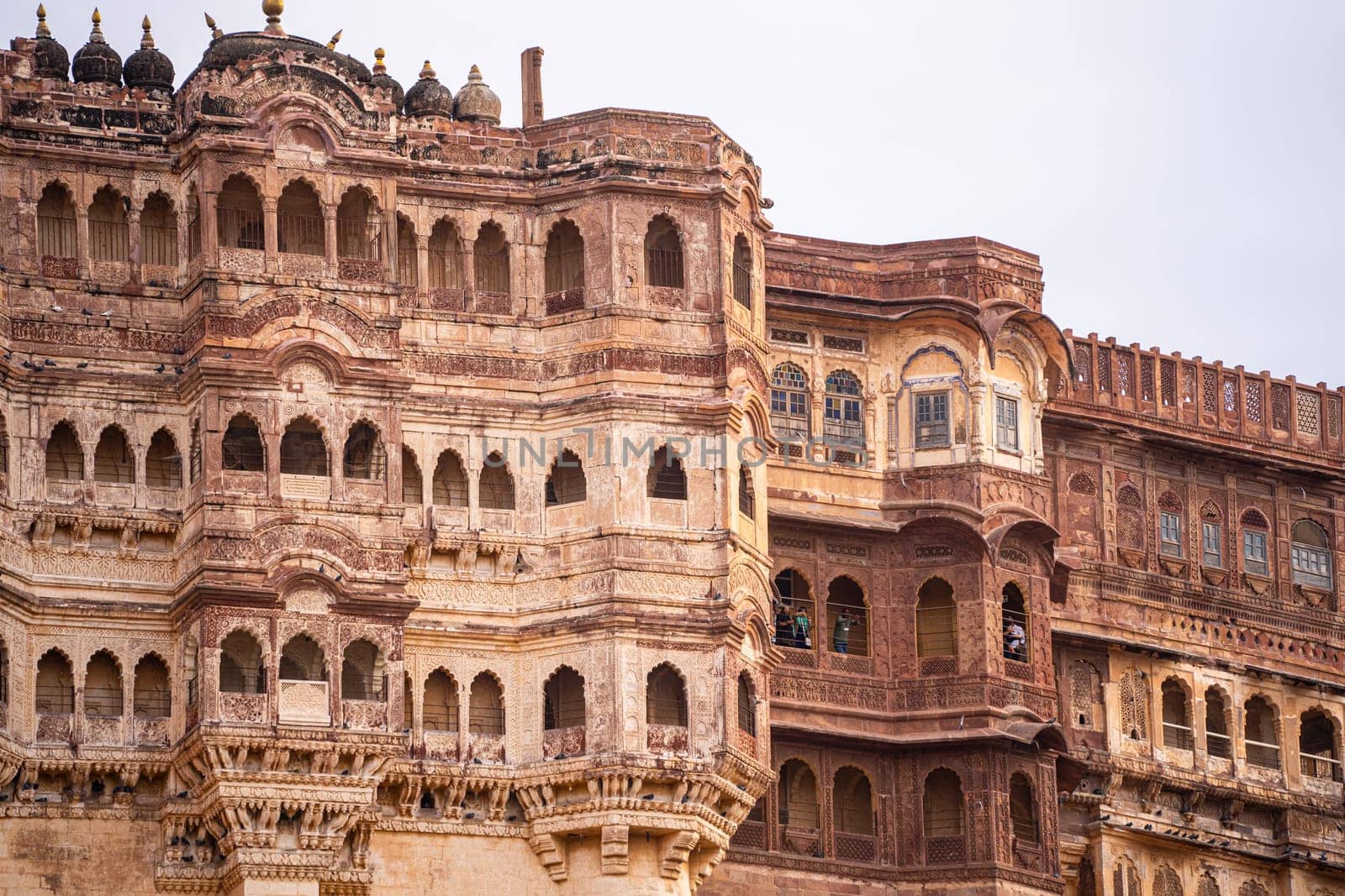 majestic stone walls of mehrangarh fort with window arches in jodhpur sitting on top of hill surrounded by monsoon clouds with birds flying around this landmark of rajput warrior history by Shalinimathur