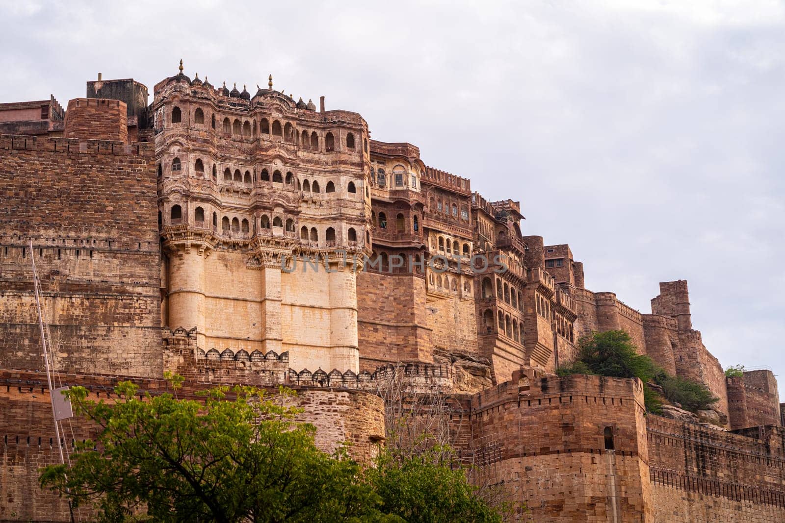 majestic stone walls of mehrangarh fort with window arches in jodhpur sitting on top of hill surrounded by monsoon clouds with birds flying around this landmark of rajput warrior history India
