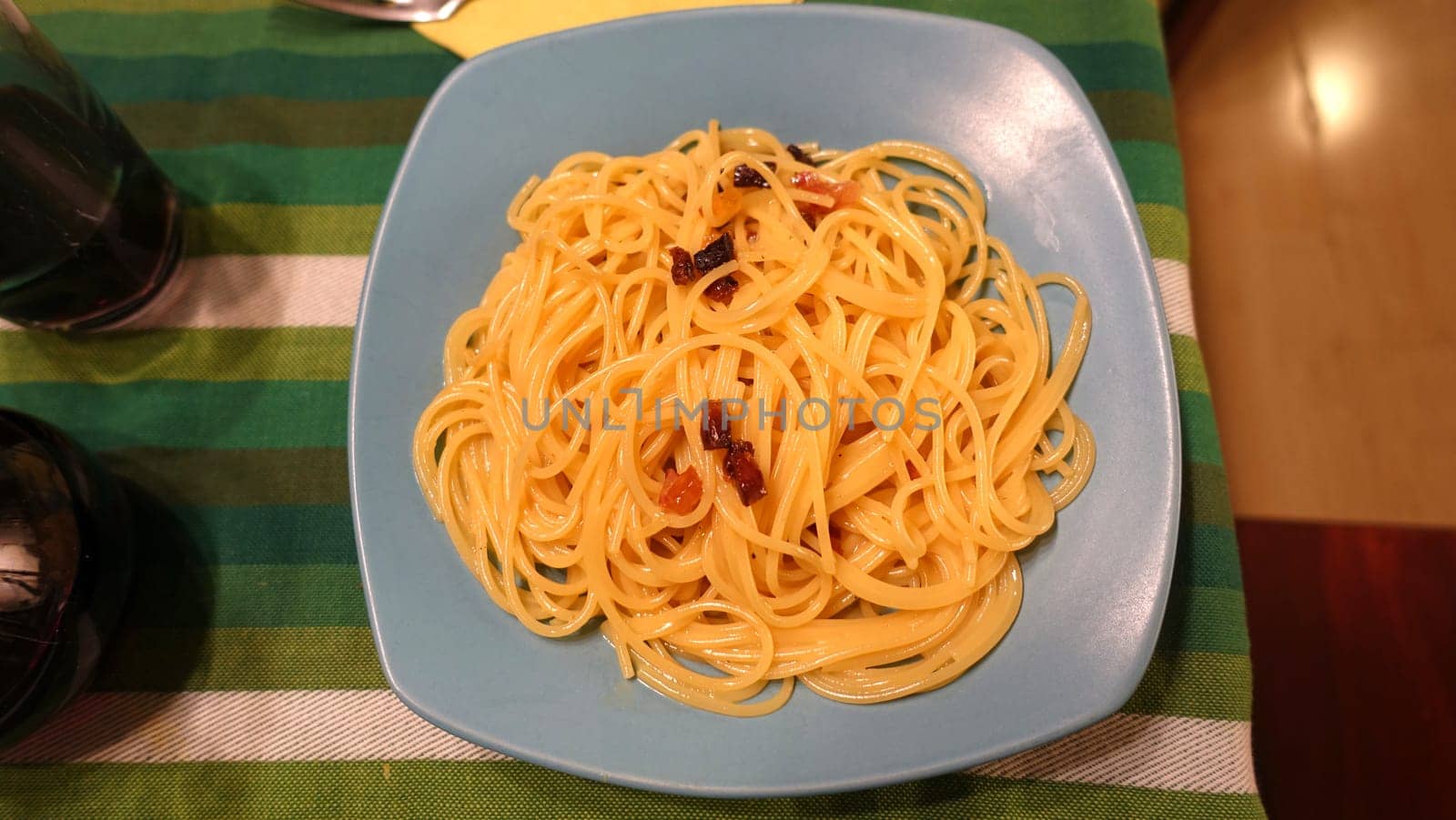A plate of spaghetti carbonara ready at the table with a quarter of red wine.