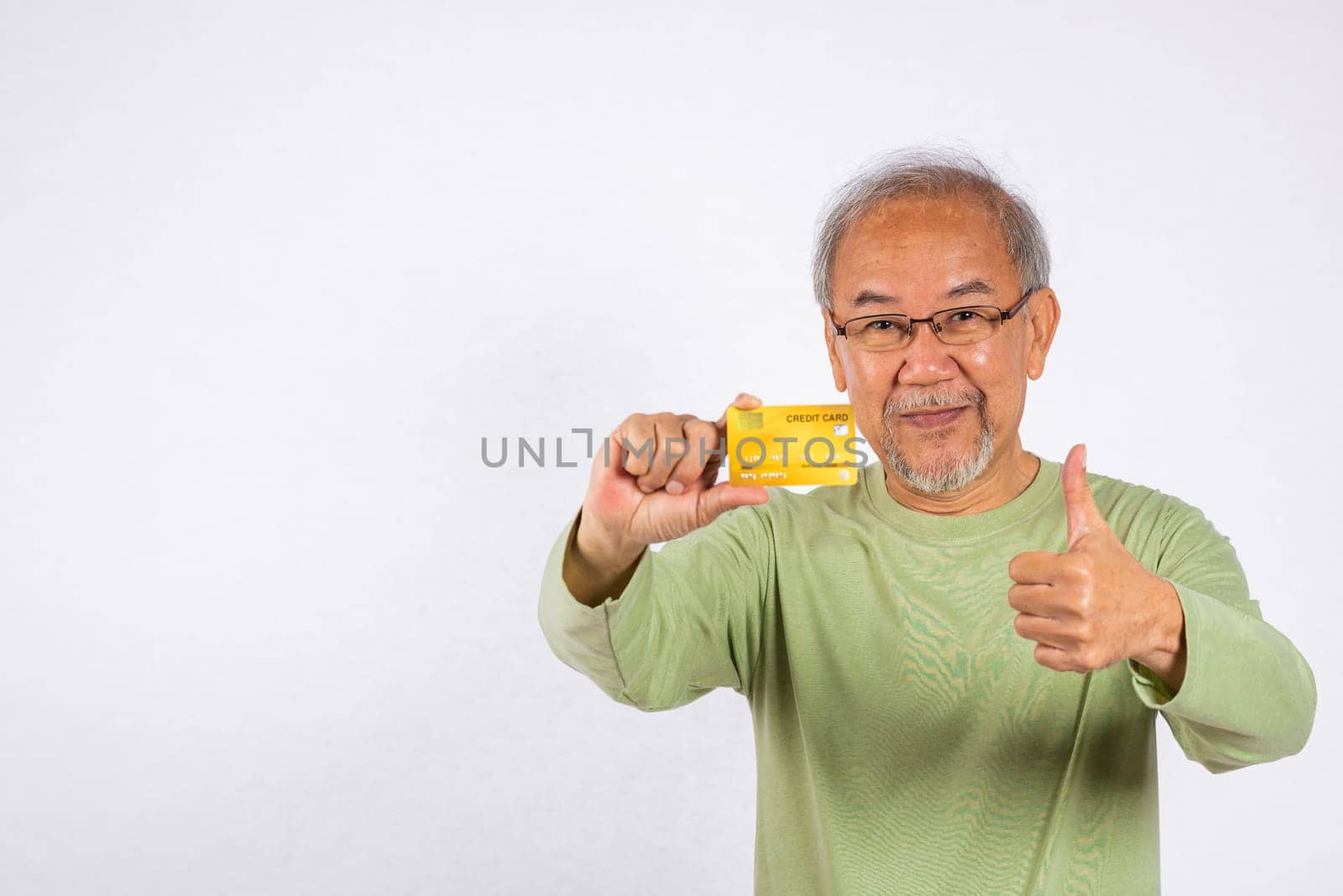 Portrait Asian smiling old man is holding credit card and giving a thumbs up for good sign studio shot isolated on white background. happy grandfather elderly positive excited shopping online