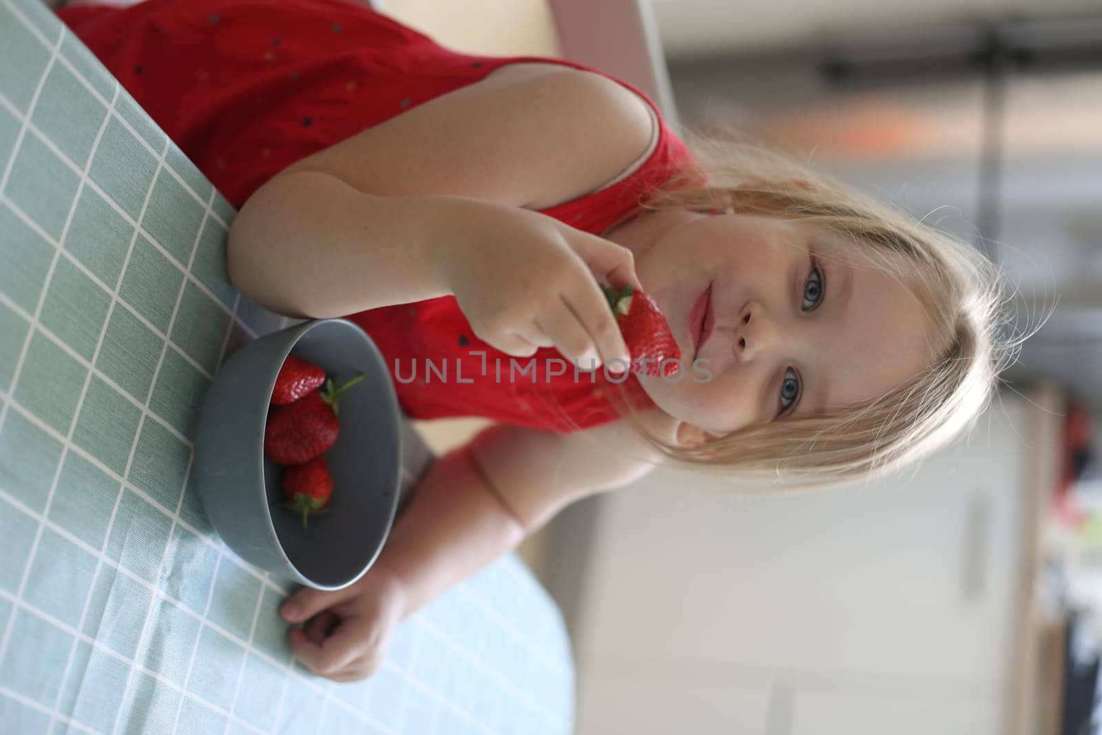 happy child girl eats strawberries in the summer home kitchen. Child enjoys a delicious berry