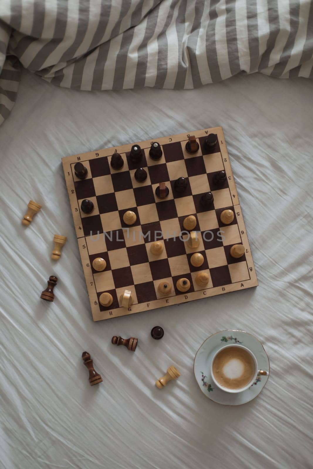 Chess board with cup of coffee on bed. Strategy thinking. Morning ideas concept. Pastel shades. High quality photo. Top view of unmade bedding sheets and pillow.