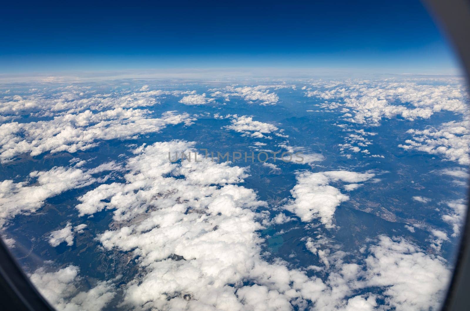 Beautiful view of white clouds over the mountainous land through the porthole window, close-up side view.