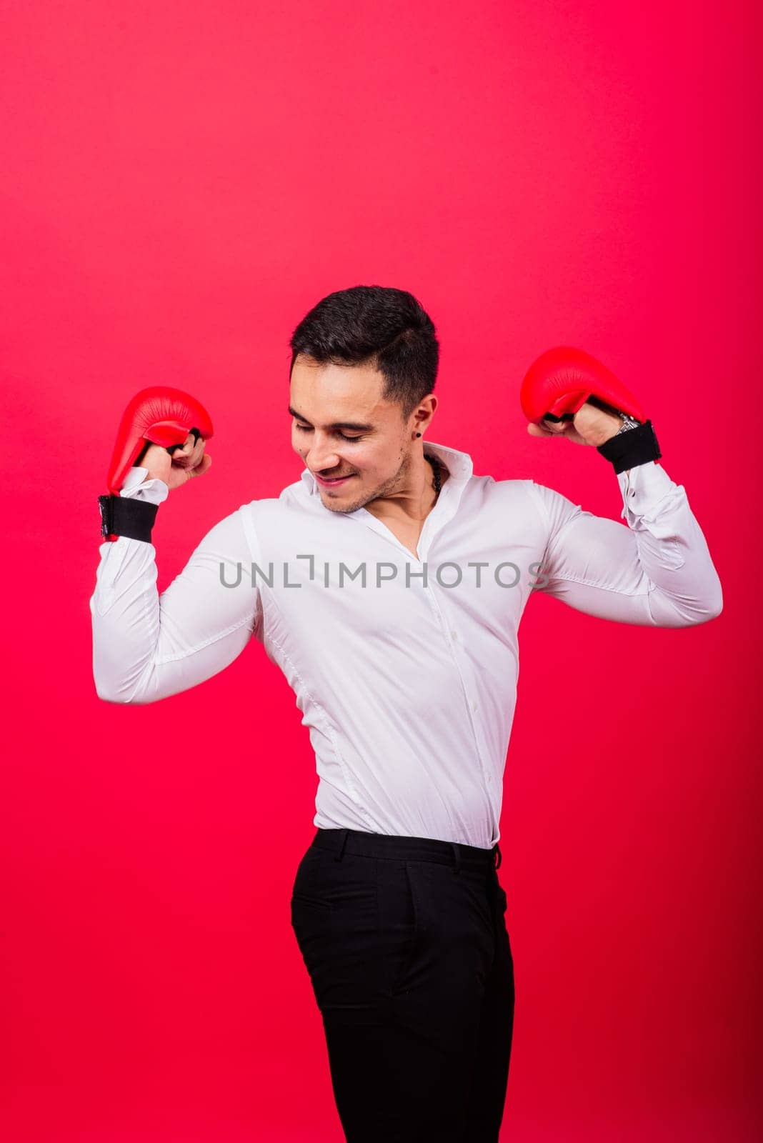 Handsome young businessman with a boxing gloves. Studio red background