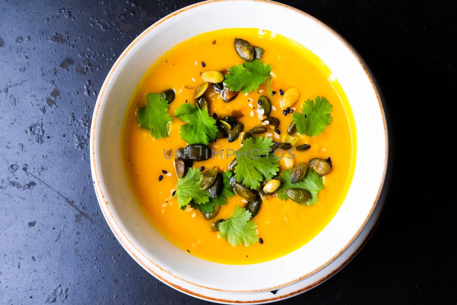 Pumpkin cream soup with parsley on a gray stone and wooden background. Top view, copy space