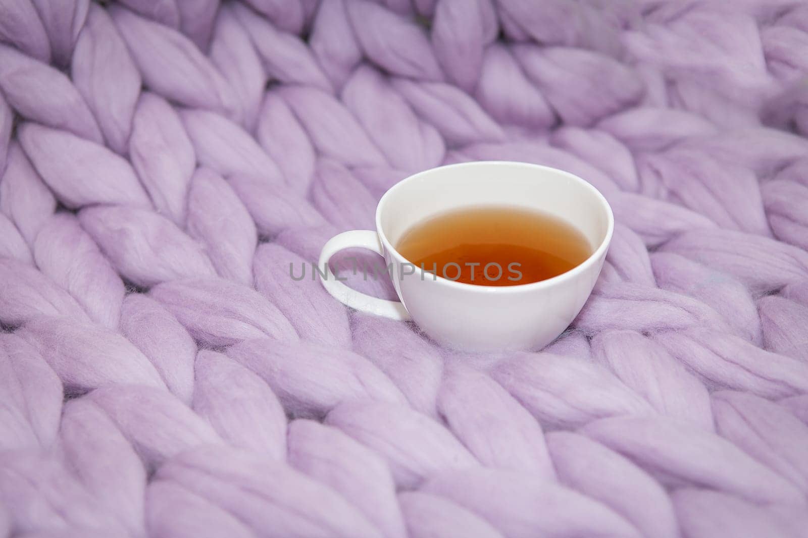 The concept of coziness and comfort is a pink-lavender knitted blanket with a white cup of hot tea on it. Place for inscription
