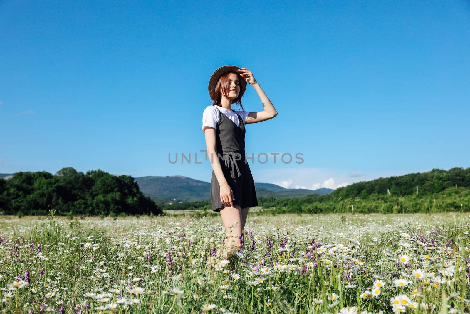 woman in a straw hat stands in a field with daisies flowers in nature