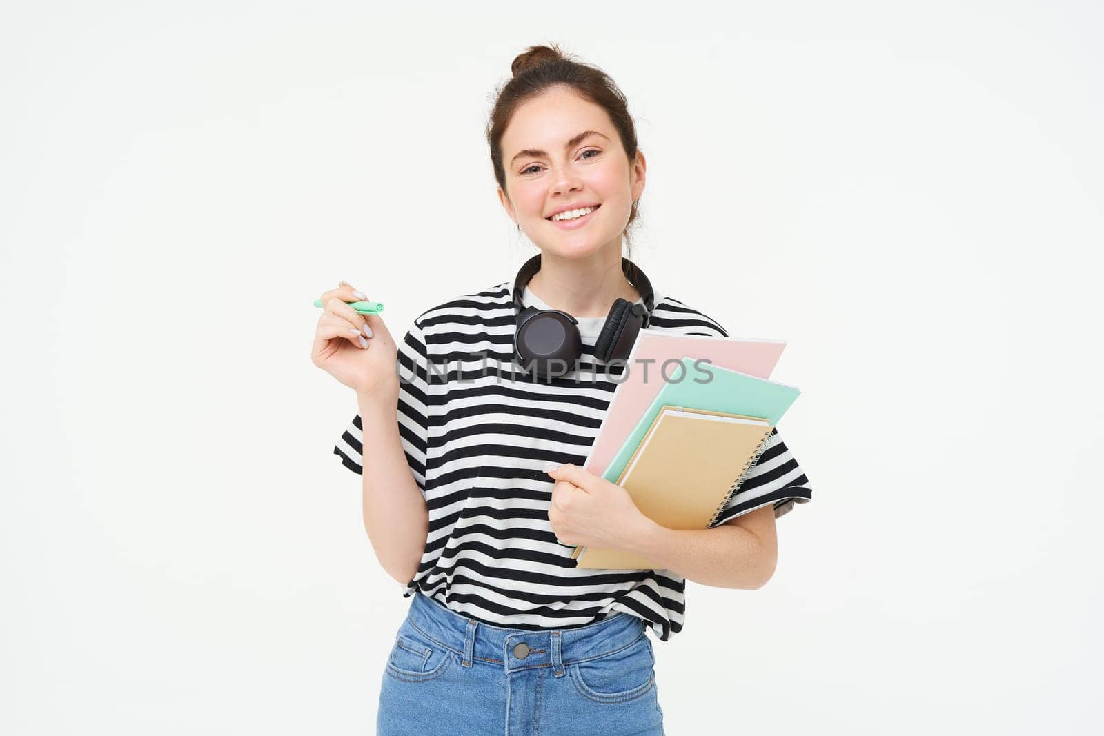 Image of young woman, tutor with books and notebooks, wearing headphones over her neck, isolated on white background. Student lifestyle concept.