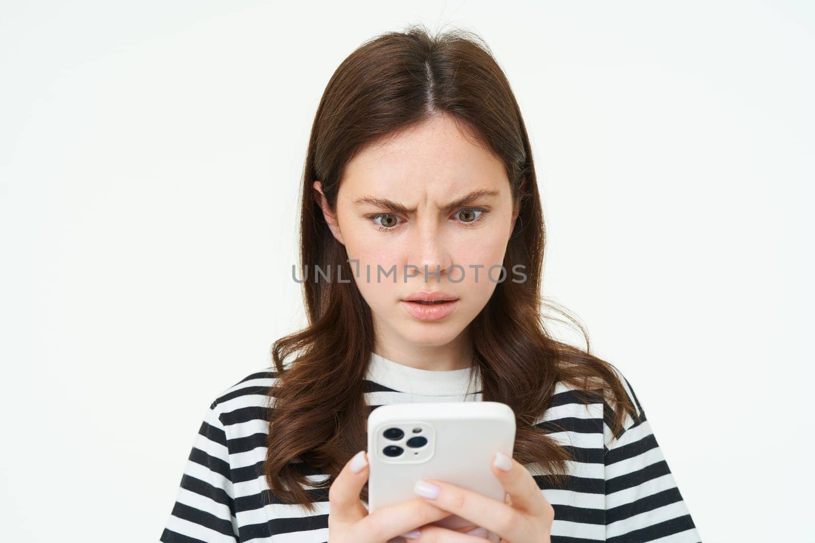 Woman looking confused and shocked at smartphone screen, frowning, reading upsetting, concerining news on mobile phone, isolated on white background.