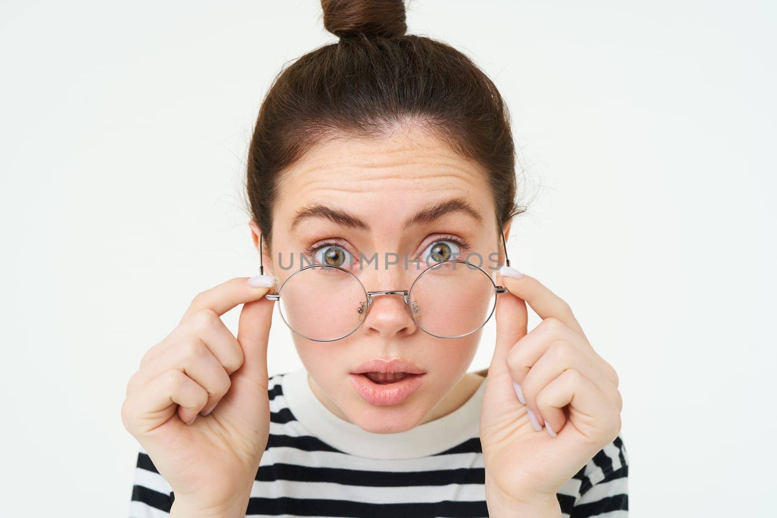 Portrait of woman leaning towards camera as if reading text with surprised face, takes off glasses, stands over white background. Copy space