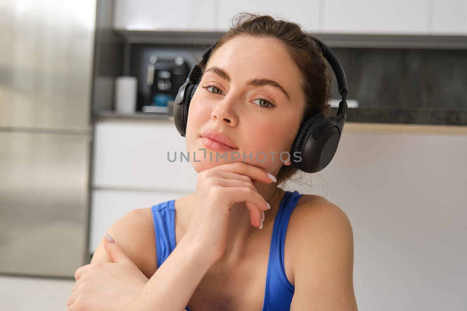 Close up portrait of fitness woman, wearing sportsbra, listening music in headphones, working out at home, doing exercises for fit and healthy body.