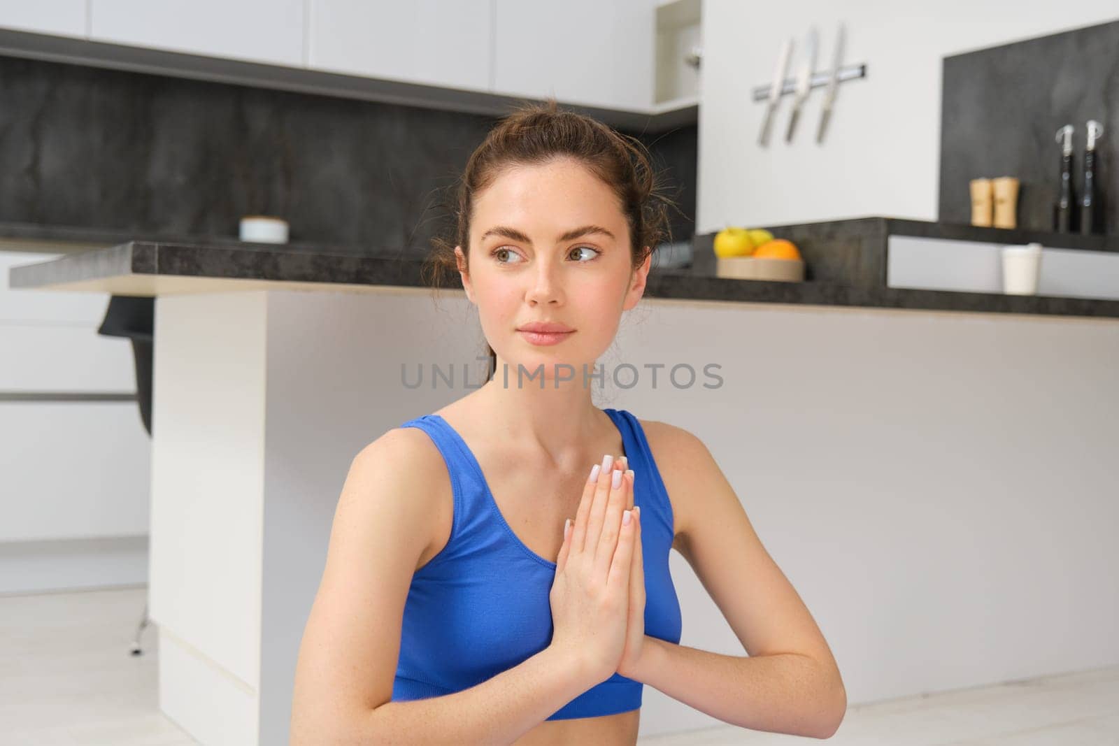 Young healthy beautiful woman in sports top and leggings practicing yoga at home, sitting in lotus position on yoga mat, meditating, smiling, relaxed, eyes closed, meditation concept by Benzoix