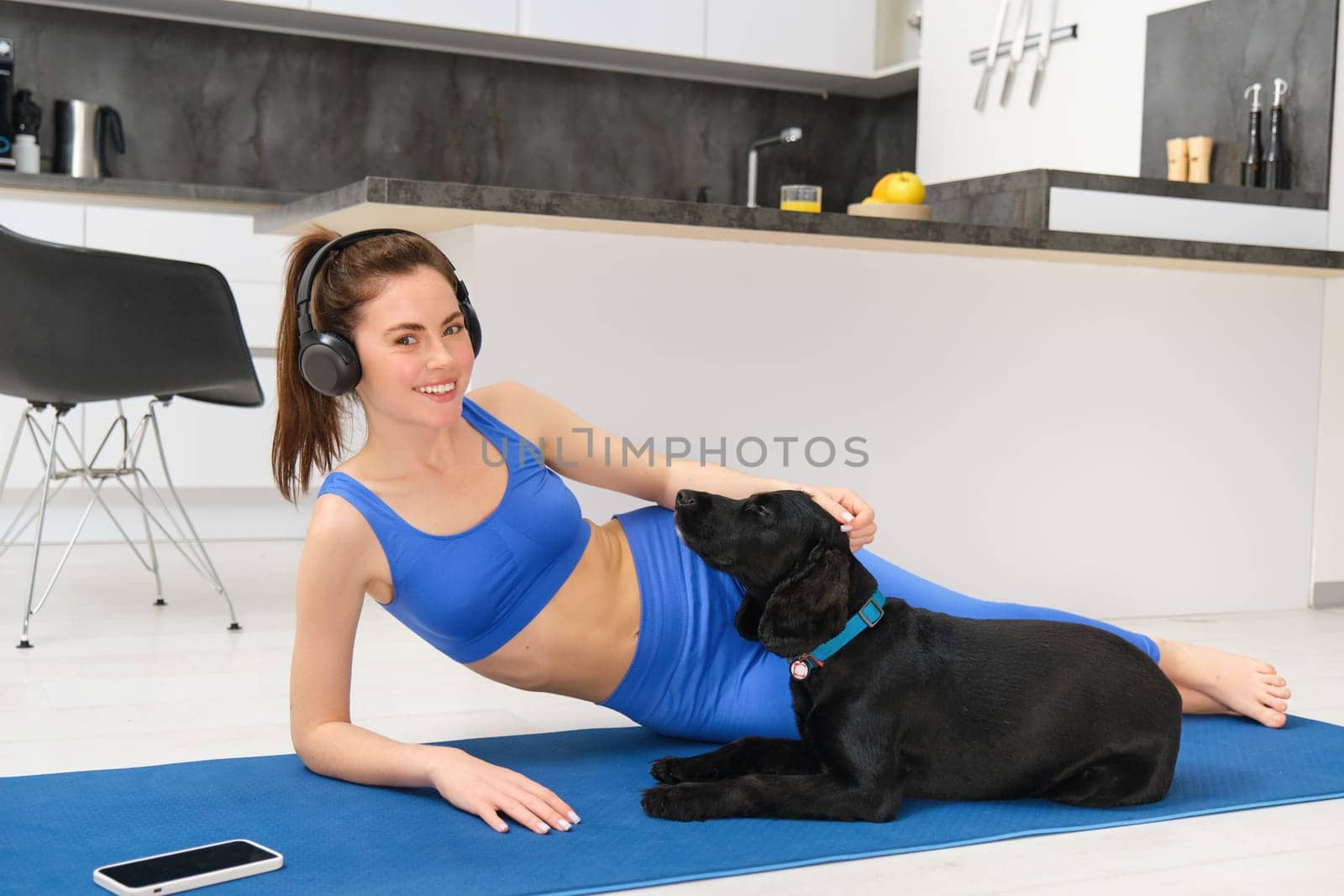 Portrait of beautiful young fitness woman, laying on yoga mat , workout at home, playing with her dog while doing sports by Benzoix