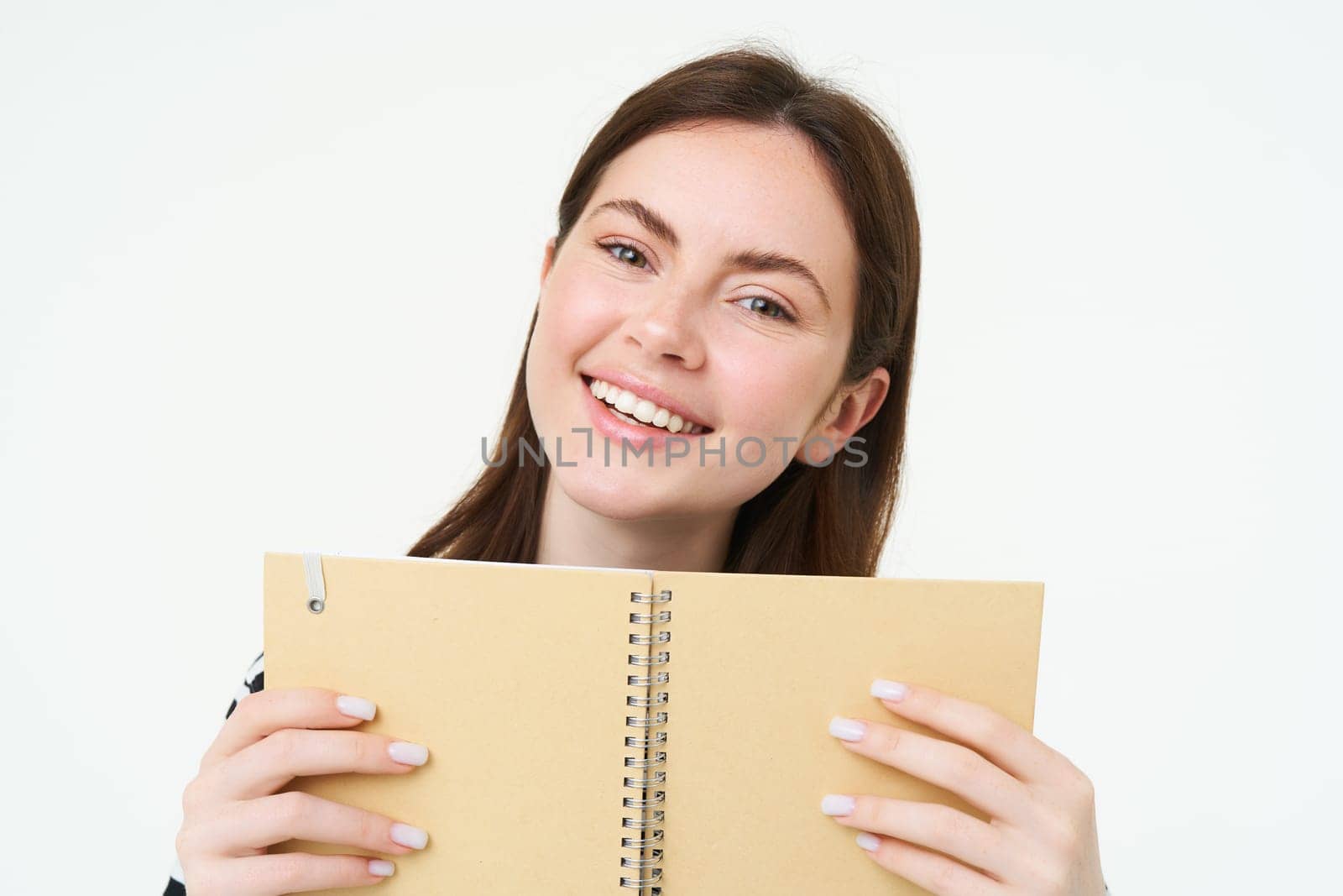 Image of young woman with notebook, holding her personal diary, work planner, smiling, reading something, standing over white background.
