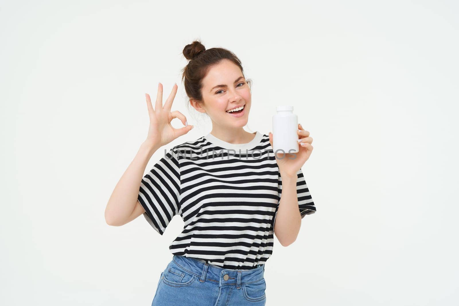 Image of smiling girl recommends dietary supplement, bottle with vitamin c, fish oil treatment, stands over white background.