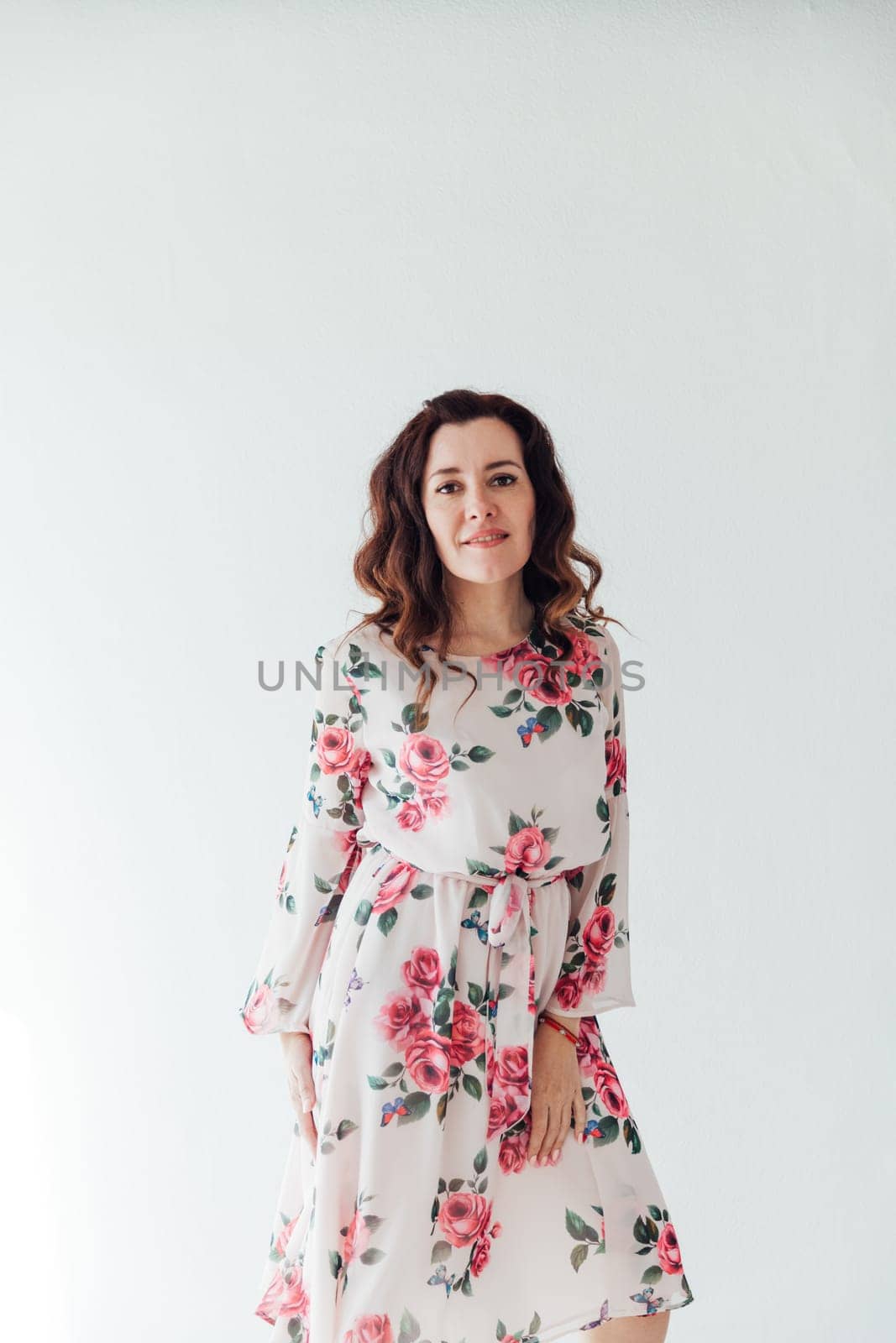 a woman in floral dress stands against a white wall on a white background