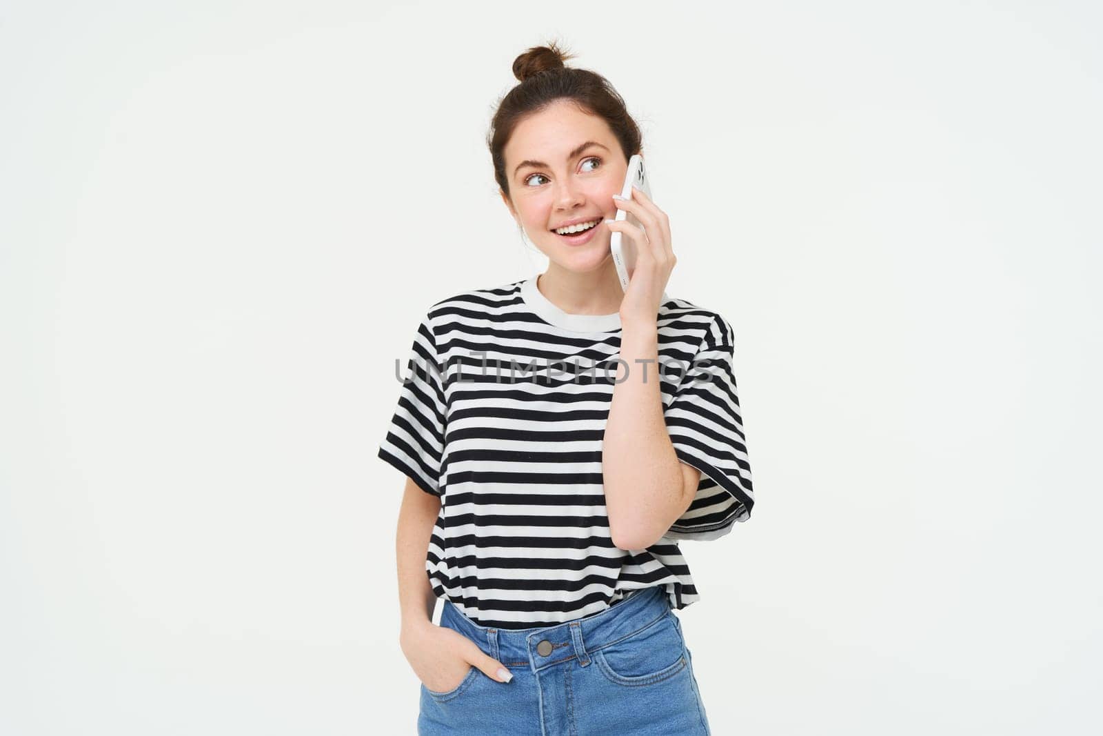 Happy young woman talks on mobile phone, chats on telephone, uses smartphone, stands over white background by Benzoix