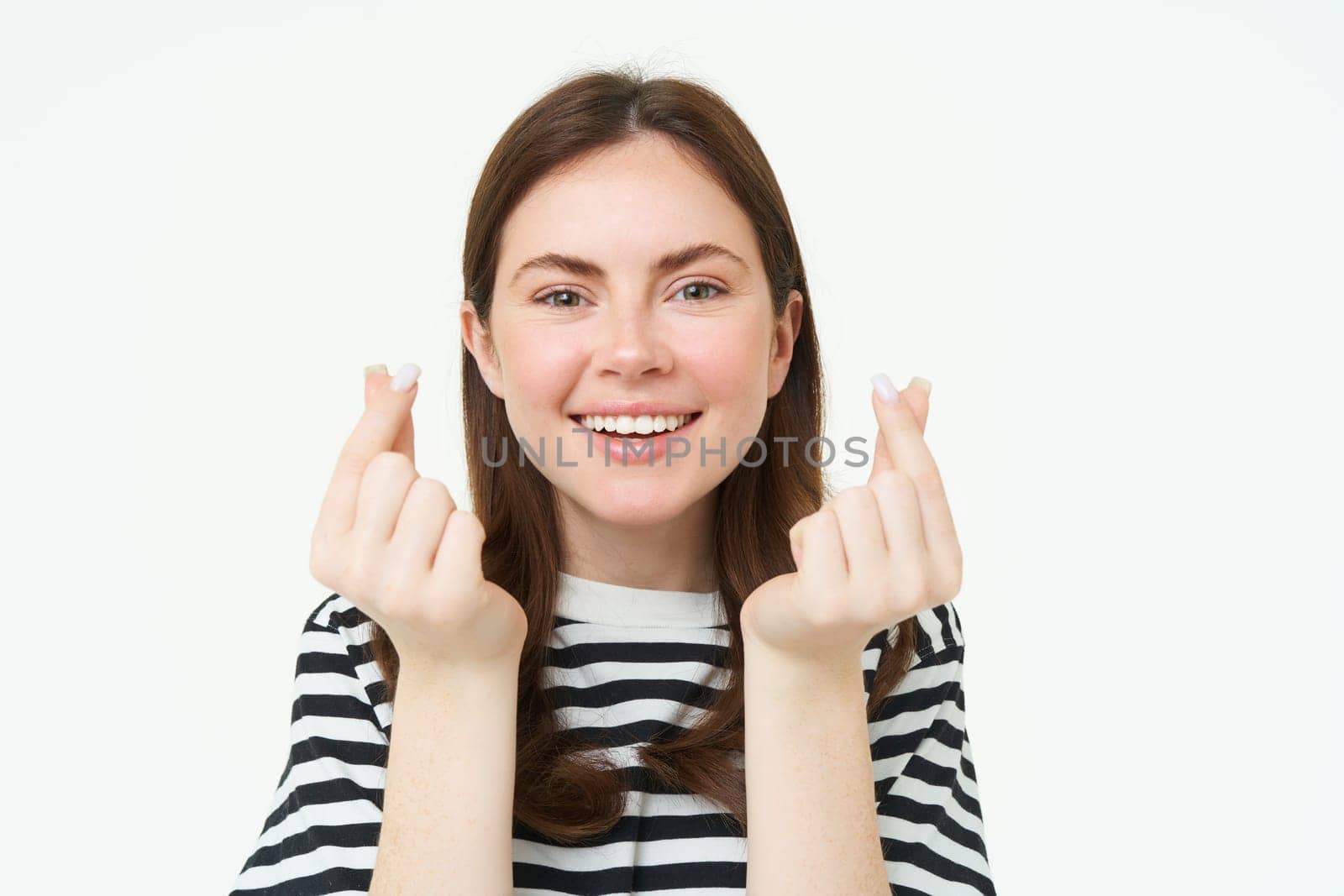 Portrait of cute young brunette woman, shows kawaii finger hearts and smiling, likes smth, stands in striped t-shirt over white background by Benzoix