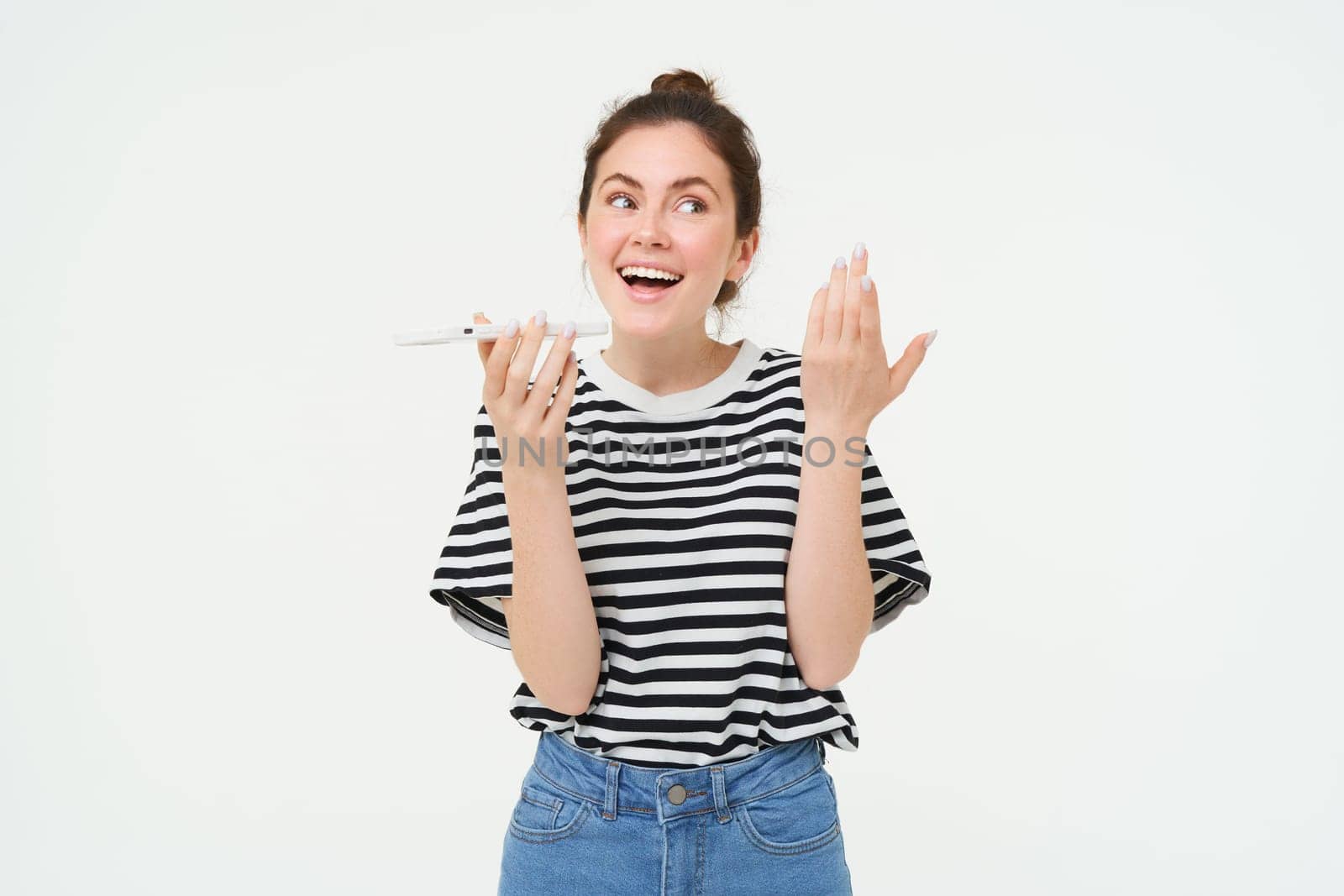 Image of chatty, happy young woman talking on mobile phone, recording voice message, explaining something over the telephone, white background.