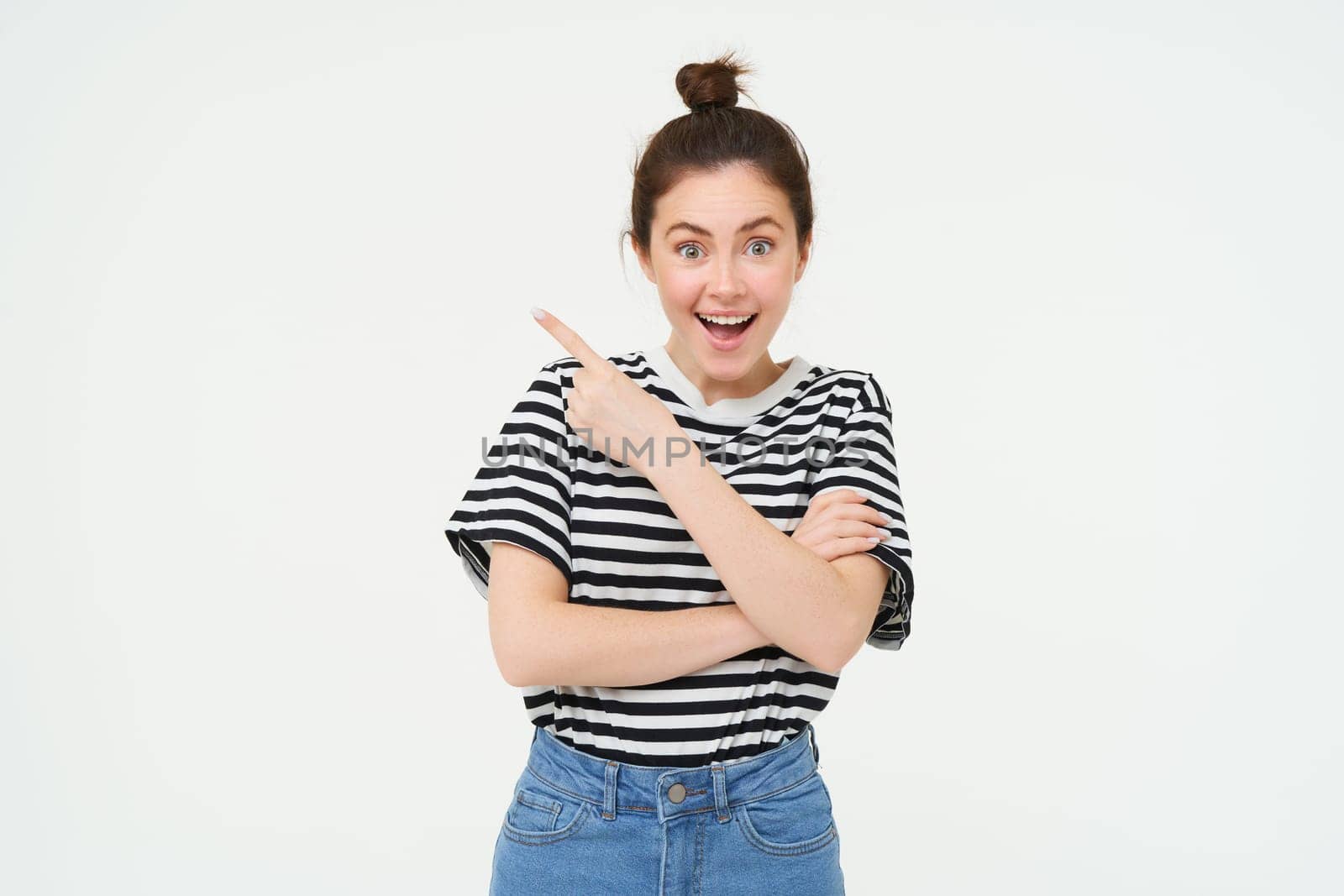 Image of excited young woman, smiling, showing amazing price discounts, pointing left, demonstrating something awesome, standing over white background.