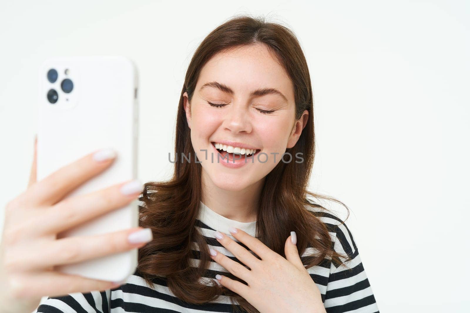 Portrait of woman laughing while taking selfie with funny photo filters, standing over white isolated background.