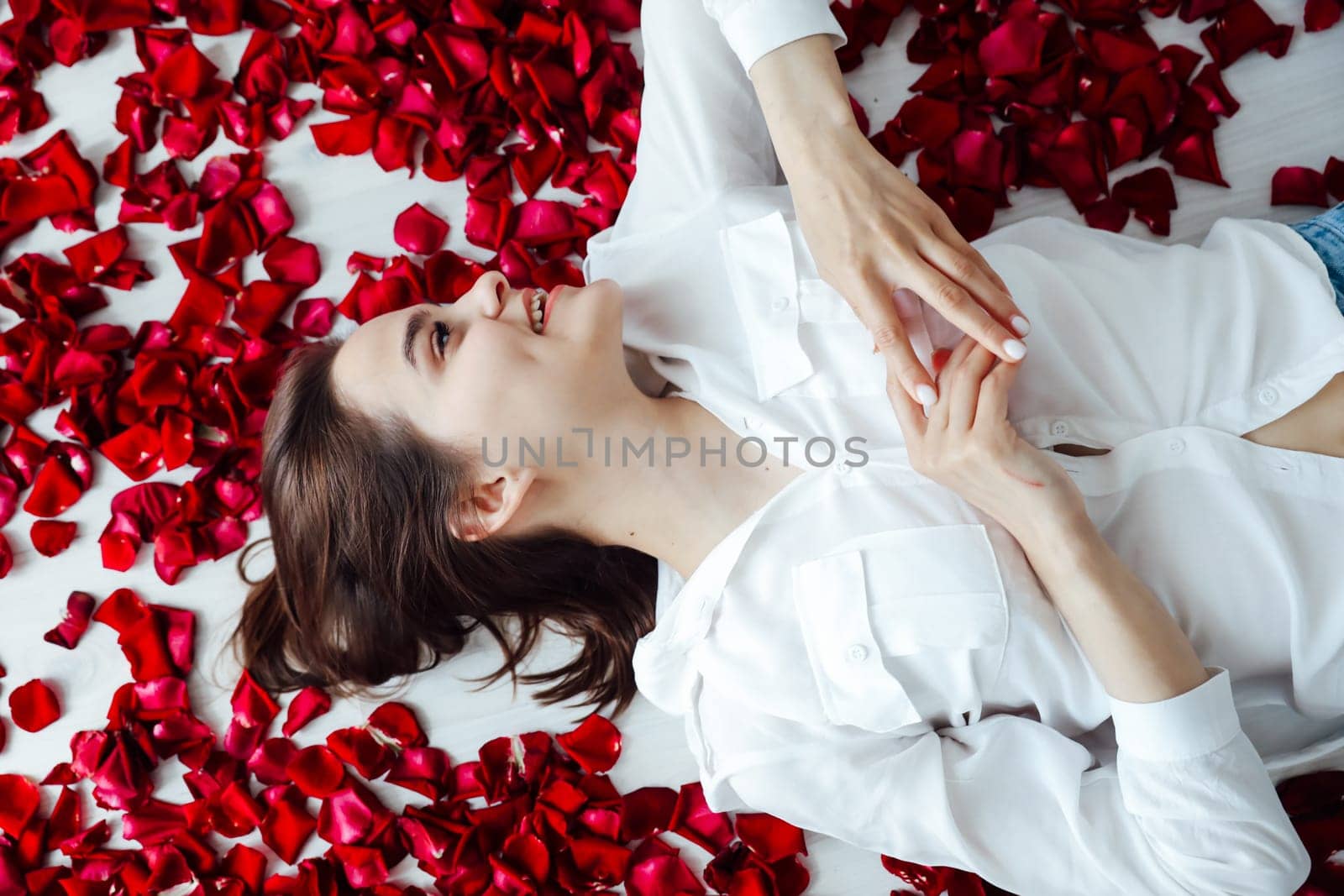 woman lies in red rose petals on the floor of the room