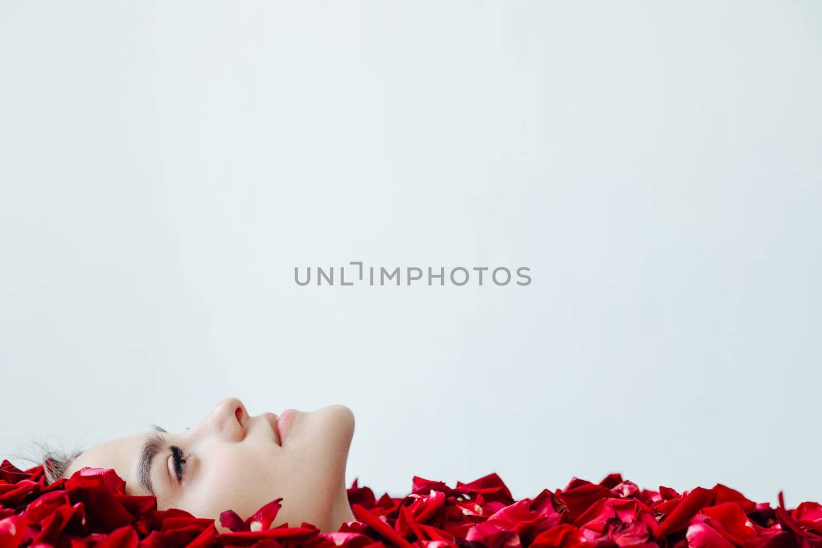 the face of woman in red rose petals on a light background