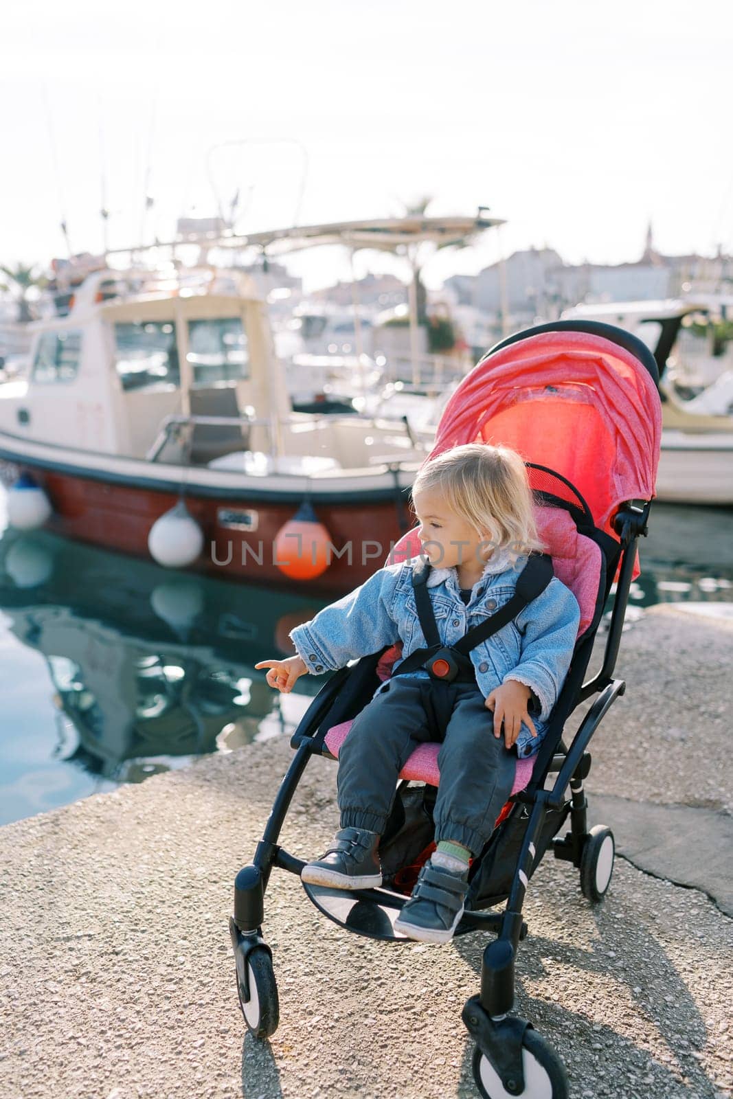 Little girl sits in a stroller on the shore and points to the sea. High quality photo