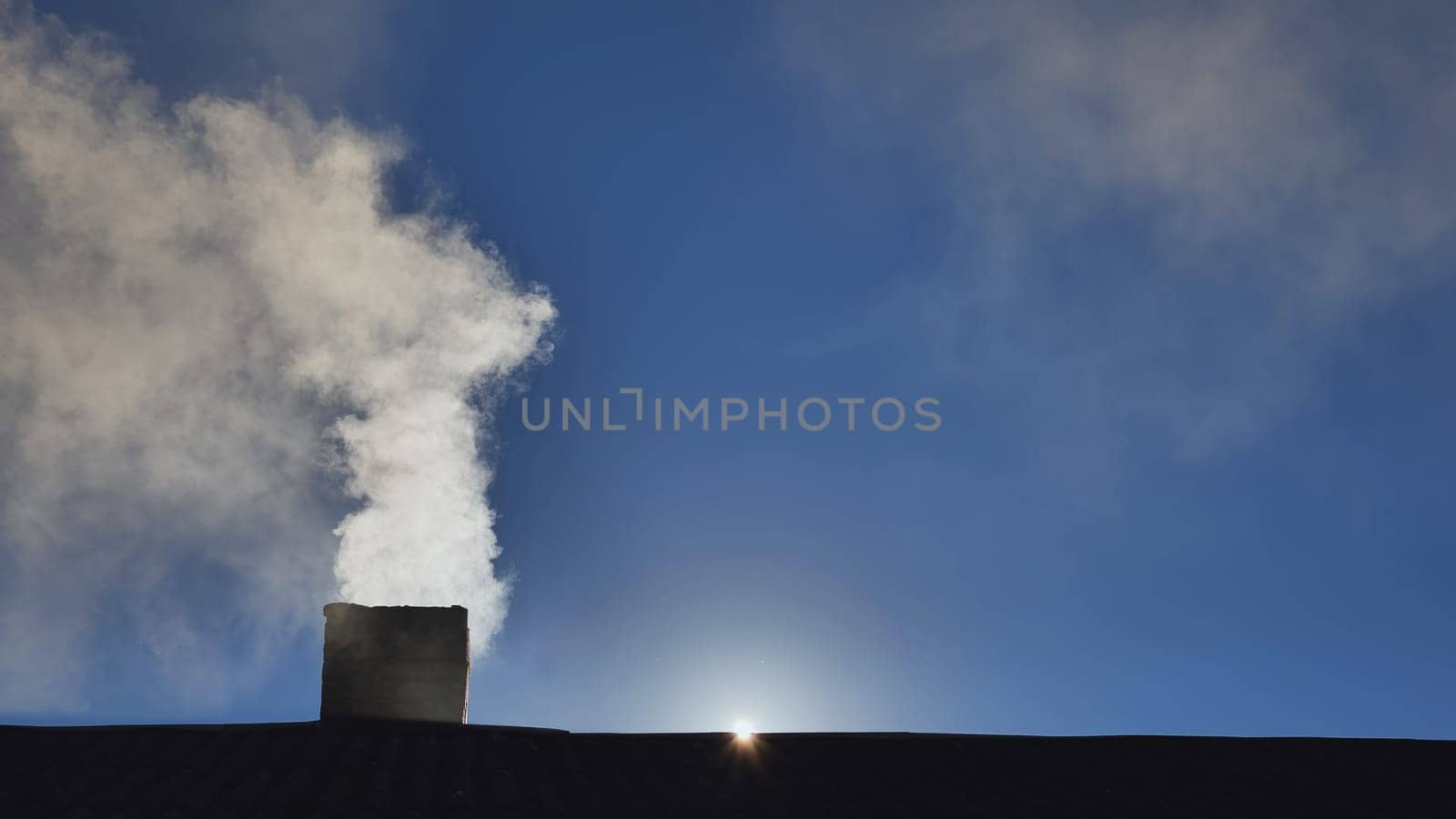 Silhouette of smoke against the sun from the chimney of a village house