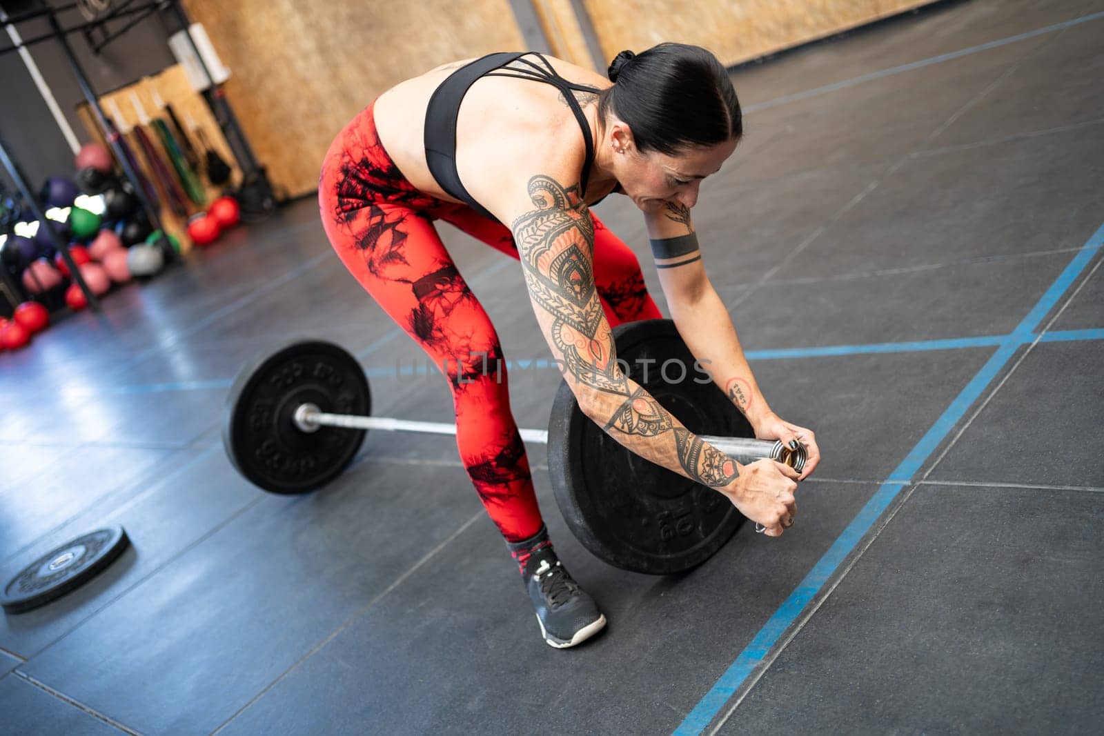 Fit mature woman preparing a bar with securing a clamp and weights to weightlifting