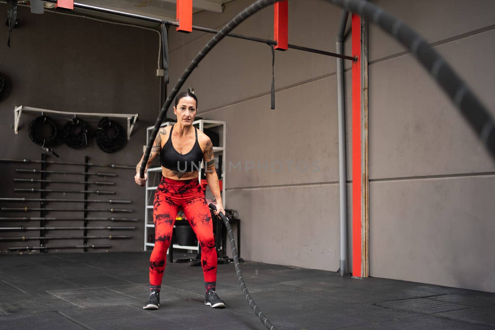 Mature strong woman exercising with battle rope in a modern cross training center