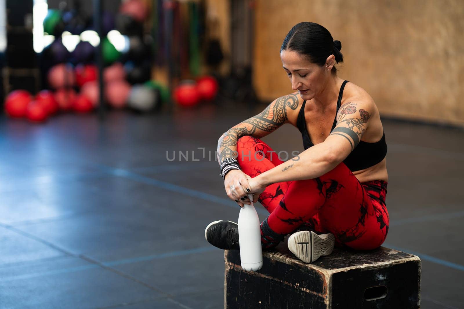 Tired woman looking down sitting on a box in gym by javiindy