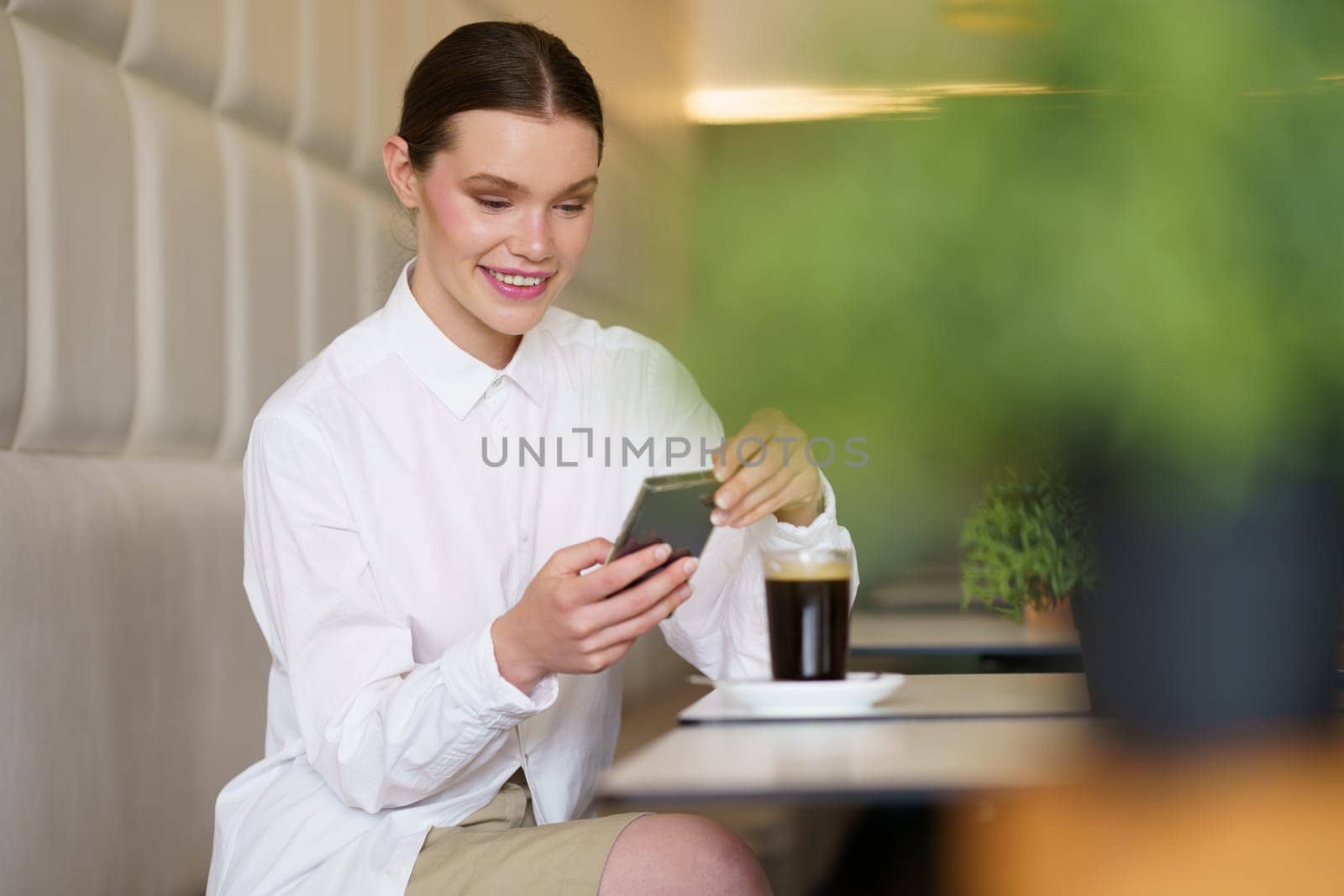 Horizontal photo with focus on a beauty chic woman using smartphone sitting on a modern cafeteria